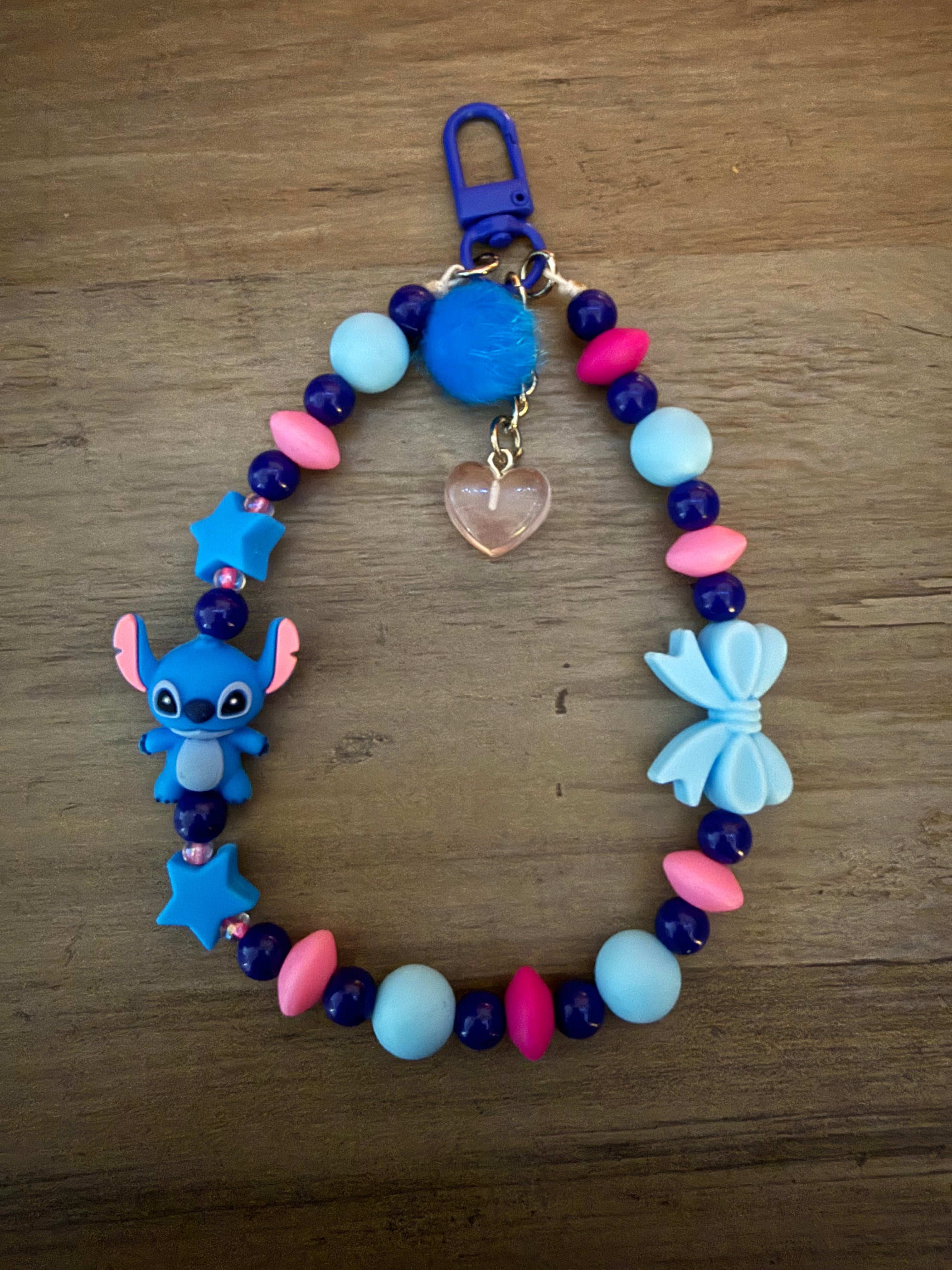 Beaded wristlet keychain with blue and pink silicone beads, featuring an alien character, blue stars, a light blue bow, a blue pom-pom, and a translucent heart charm.