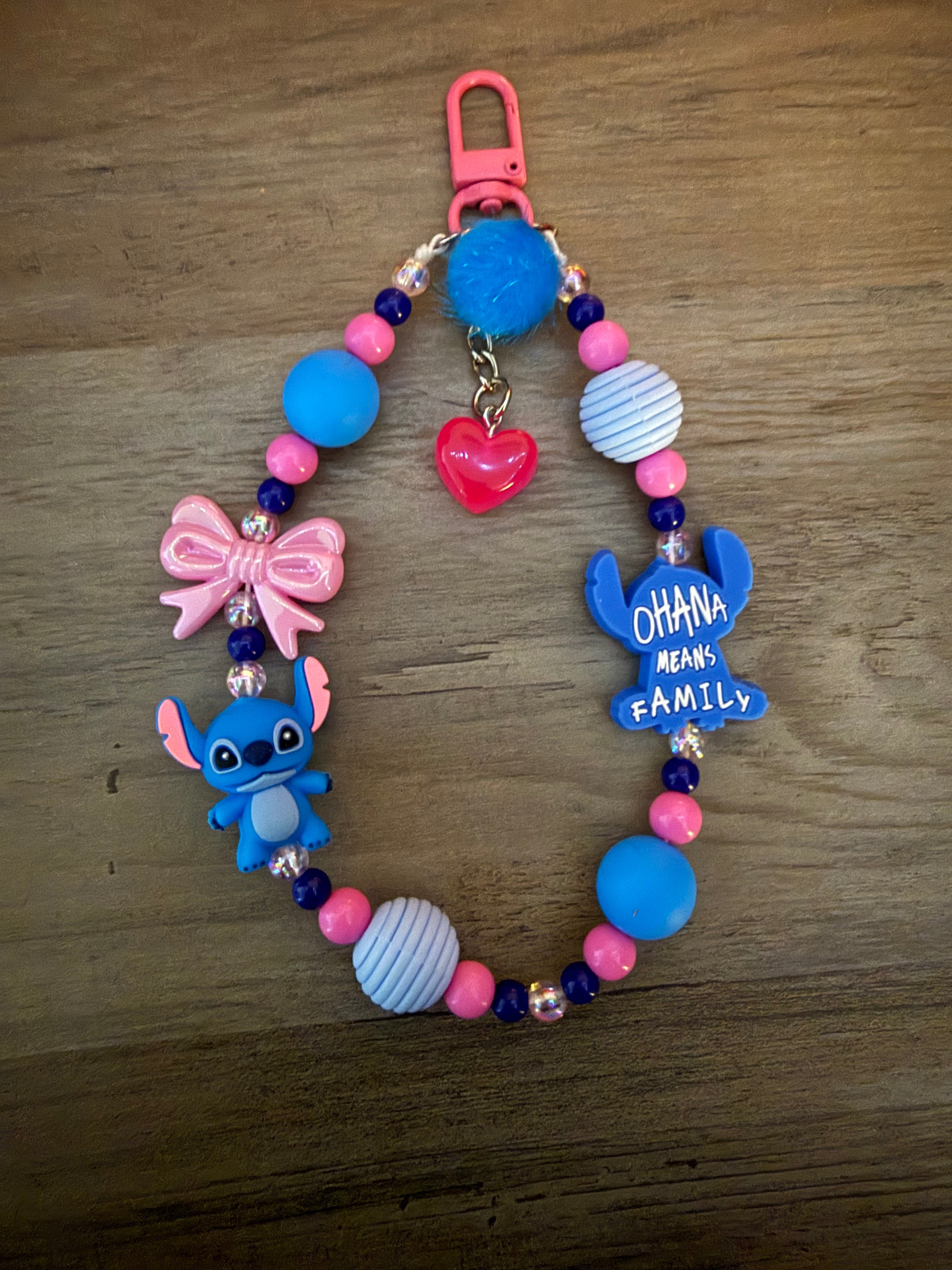 A beaded Stitch-themed keychain loop featuring a small alien figure, a pink bow, a "Ohana means family" charm, and a pink heart.