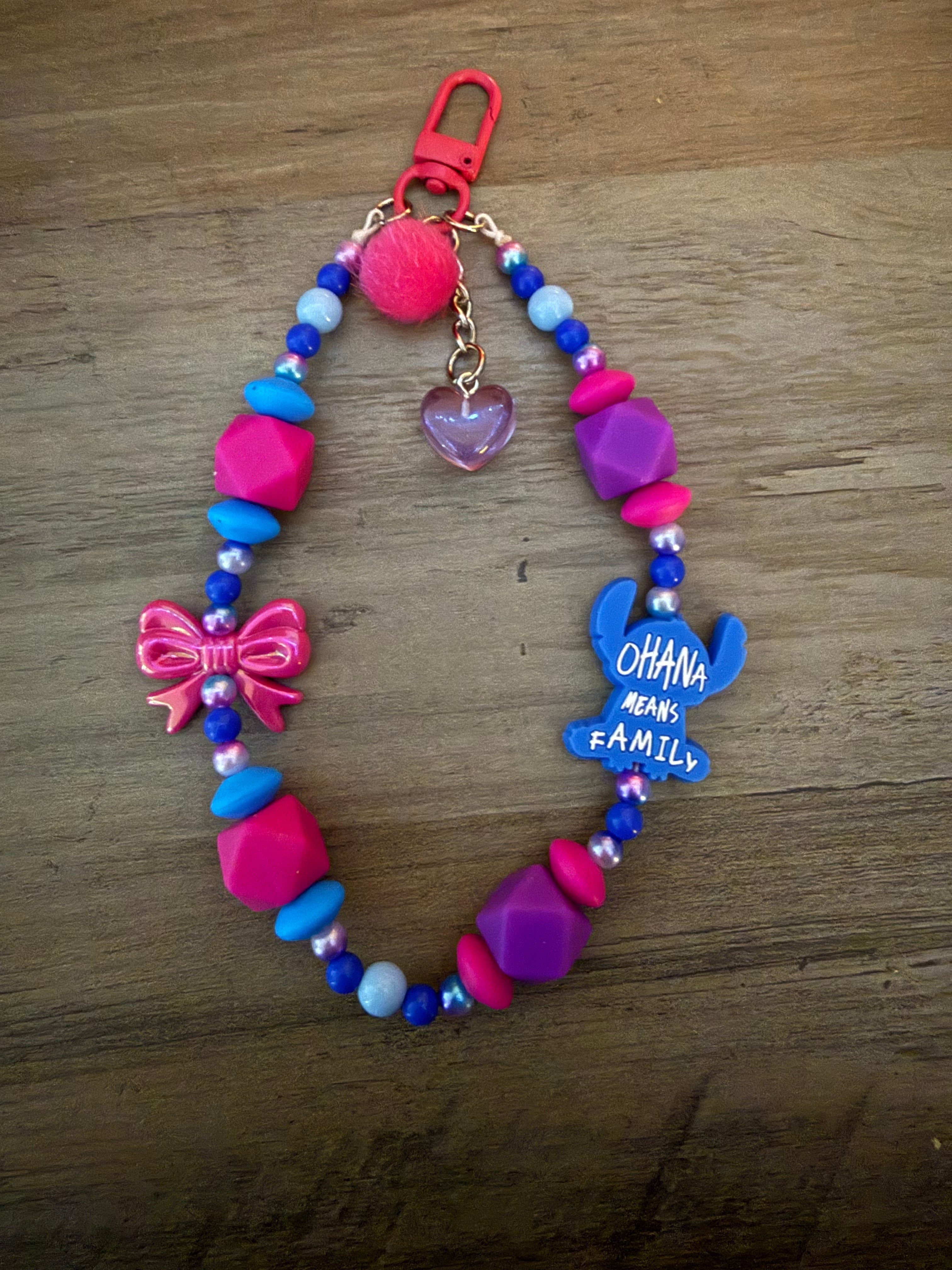 Beaded wristlet keychain with pink, purple, and blue beads, featuring a pink bow, a "Alien" silhouette with the text "Ohana Means Family," a heart charm, and a pink pom-pom.