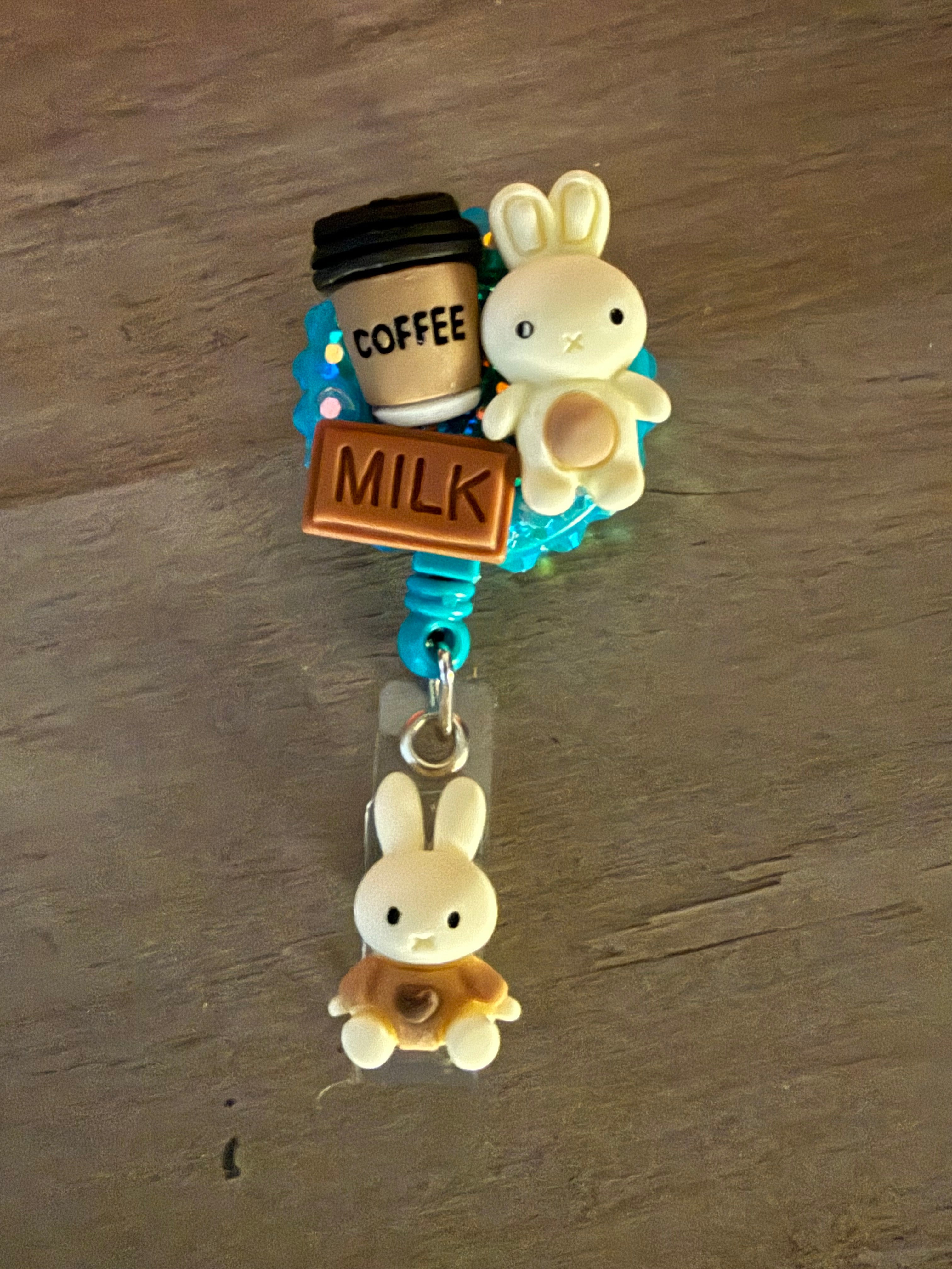 Handmade blue glitter badge reel featuring "kawaii" charms of a white bunny, a coffee cup, and a chocolate milk bar, with a matching bunny charm hanging below.
