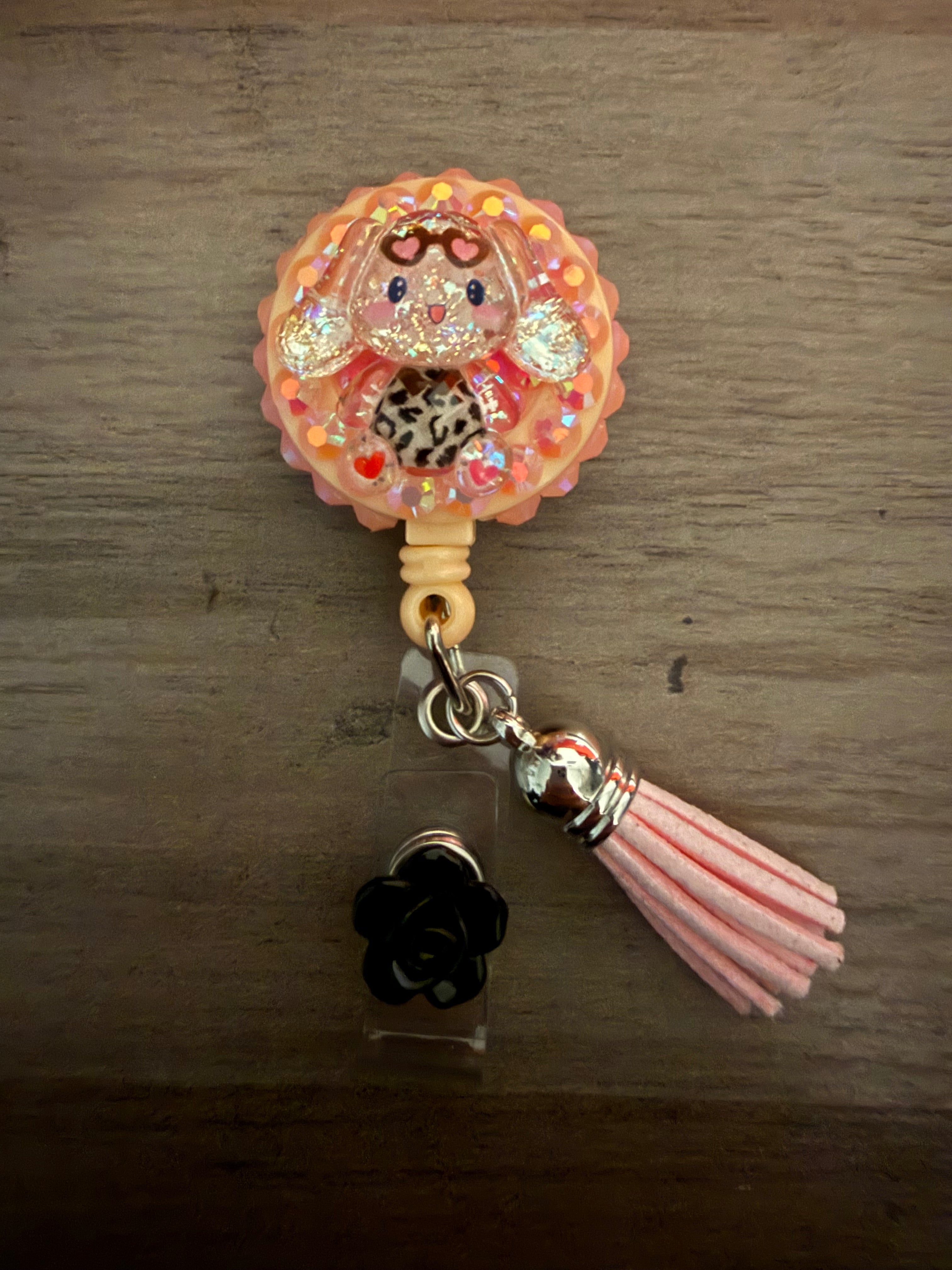 A decoden retractable badge reel featuring a glittery Cinnamoroll character in leopard print, accented with pink gems, a pink tassel, and a black flower charm.