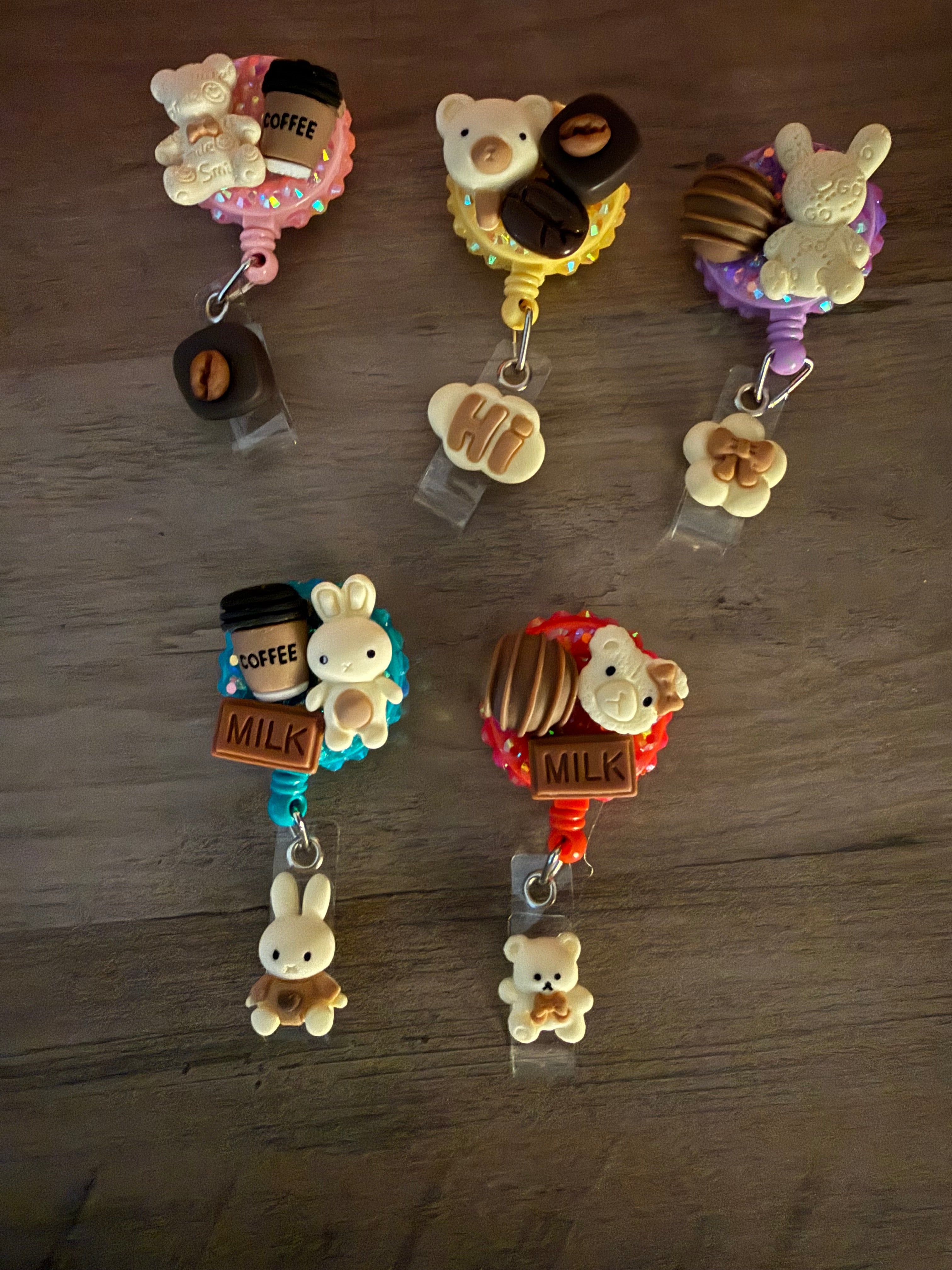 Five retractable badge reels decorated in a decoden style with charms of bears, bunnies, coffee cups, and chocolate bars on colorful, glittery bases.