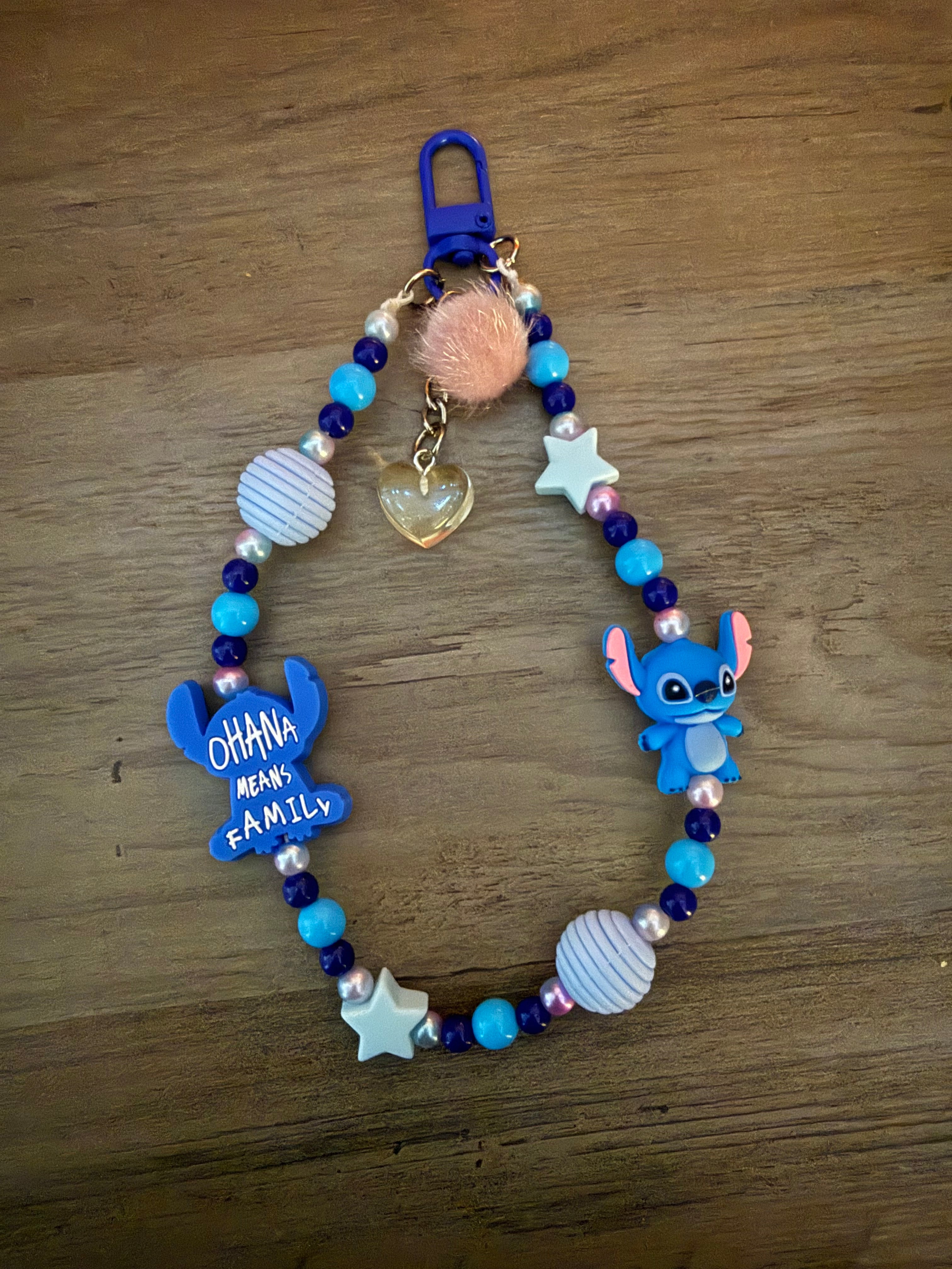 Beaded wristlet keychain in shades of blue, featuring alien characters, "Ohana Means Family" charm, white stars, a peach pom-pom, and a gold heart charm.