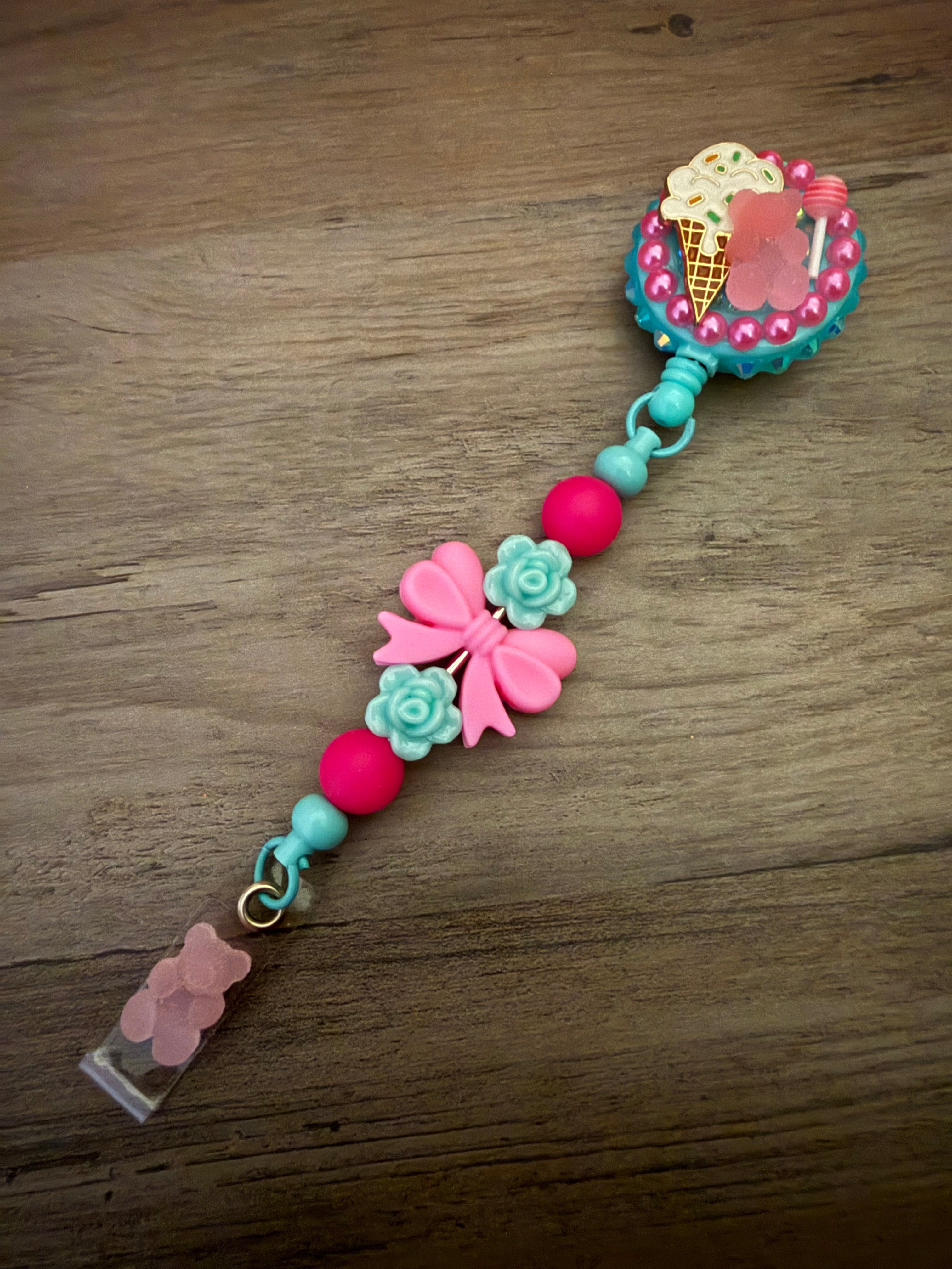 Handmade teal badge reel featuring an ice cream cone and pink gummy bear charm, accented by a decorative beaded lanyard with a pink bow, teal roses, and a matching pink gummy bear dangle.