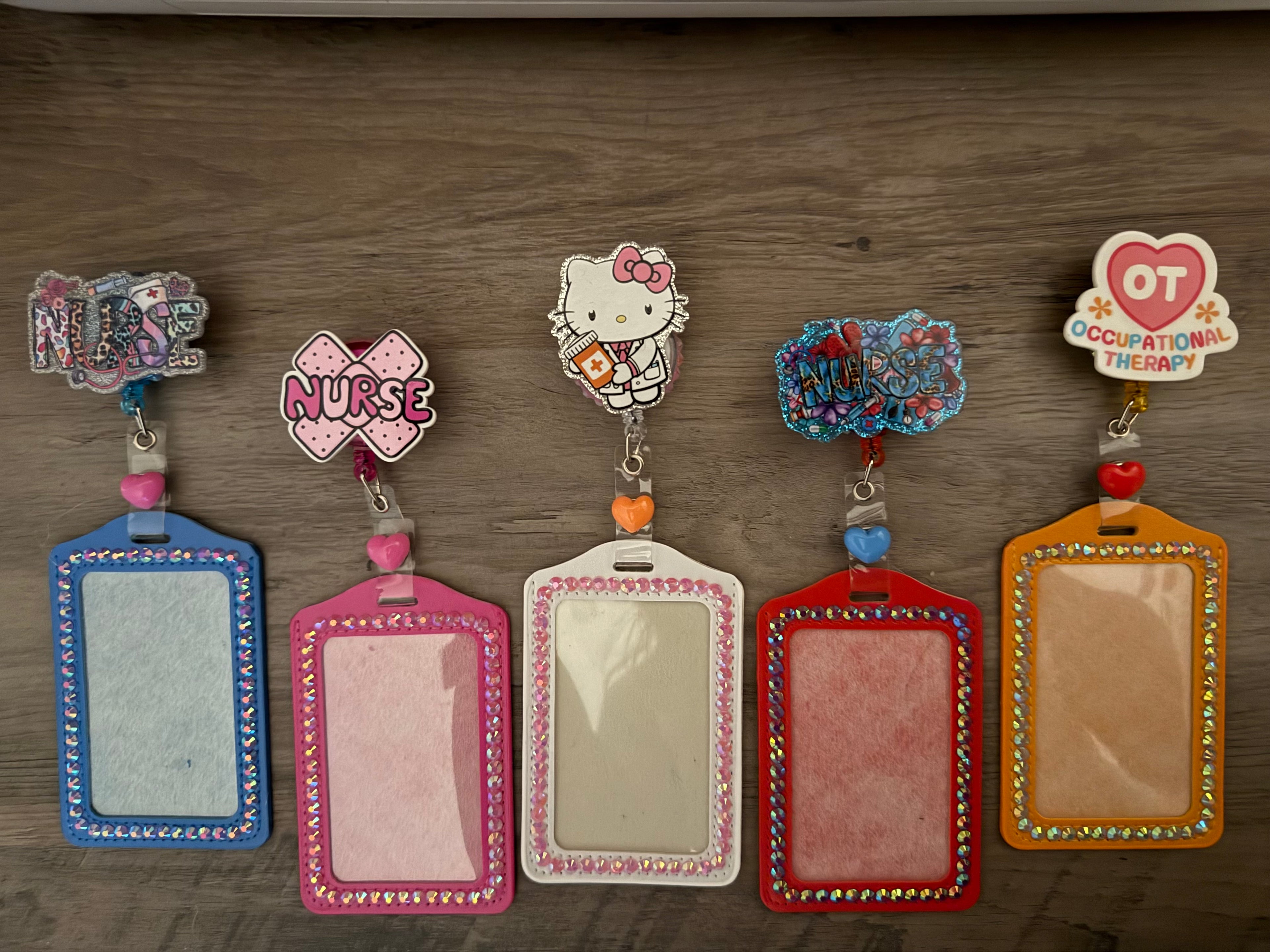 Five glittery badge reels with matching rhinestone-lined ID holders arranged in a row. The designs include medical themes like "NURSE" and "OT OCCUPATIONAL THERAPY," alongside a character in a doctor's coat, each accented with colorful heart charms and sparkling embellishments.