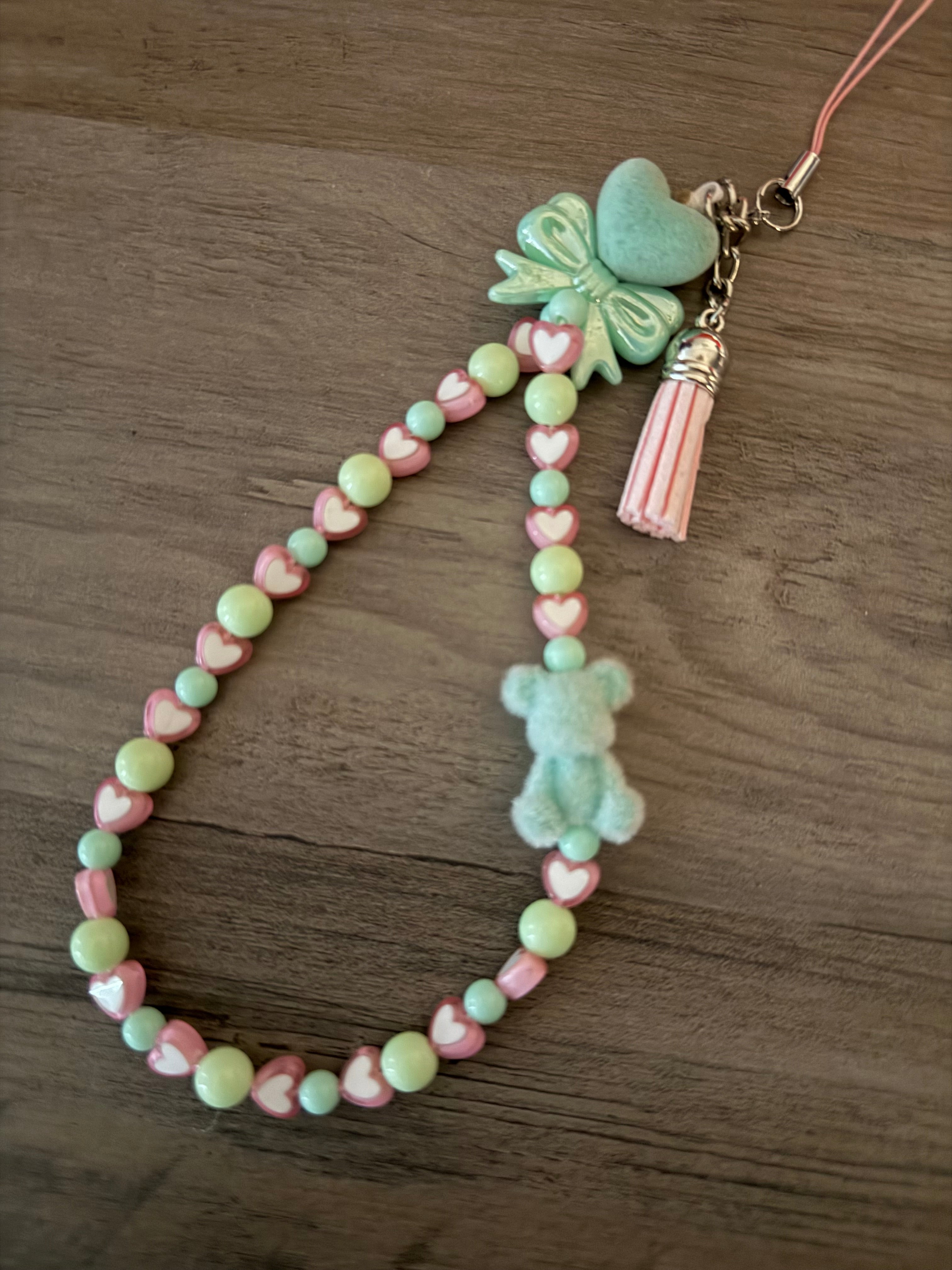 Handmade beaded phone charm featuring mint green and pink heart-shaped beads, a small fuzzy mint bear figure, a green bow, and a pink tassel