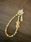 Handmade beaded phone charm featuring cream and orange beads, a small orange fuzzy bear figure, a white bow, and a cream tassel.