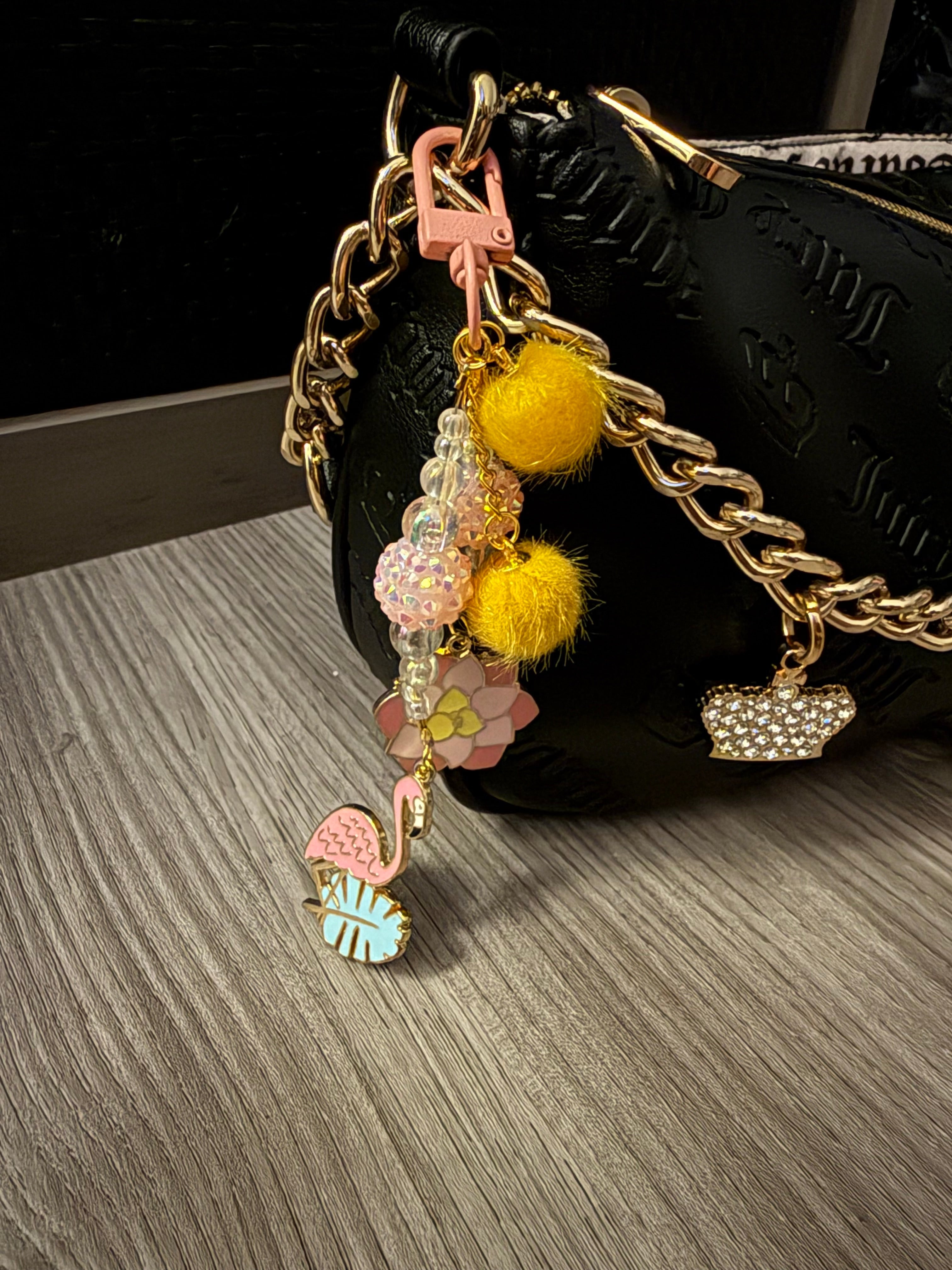 Close-up of a handcrafted bag charm featuring a light blue lobster clasp, navy and bright blue pom-poms, and gold-tone bow accents.