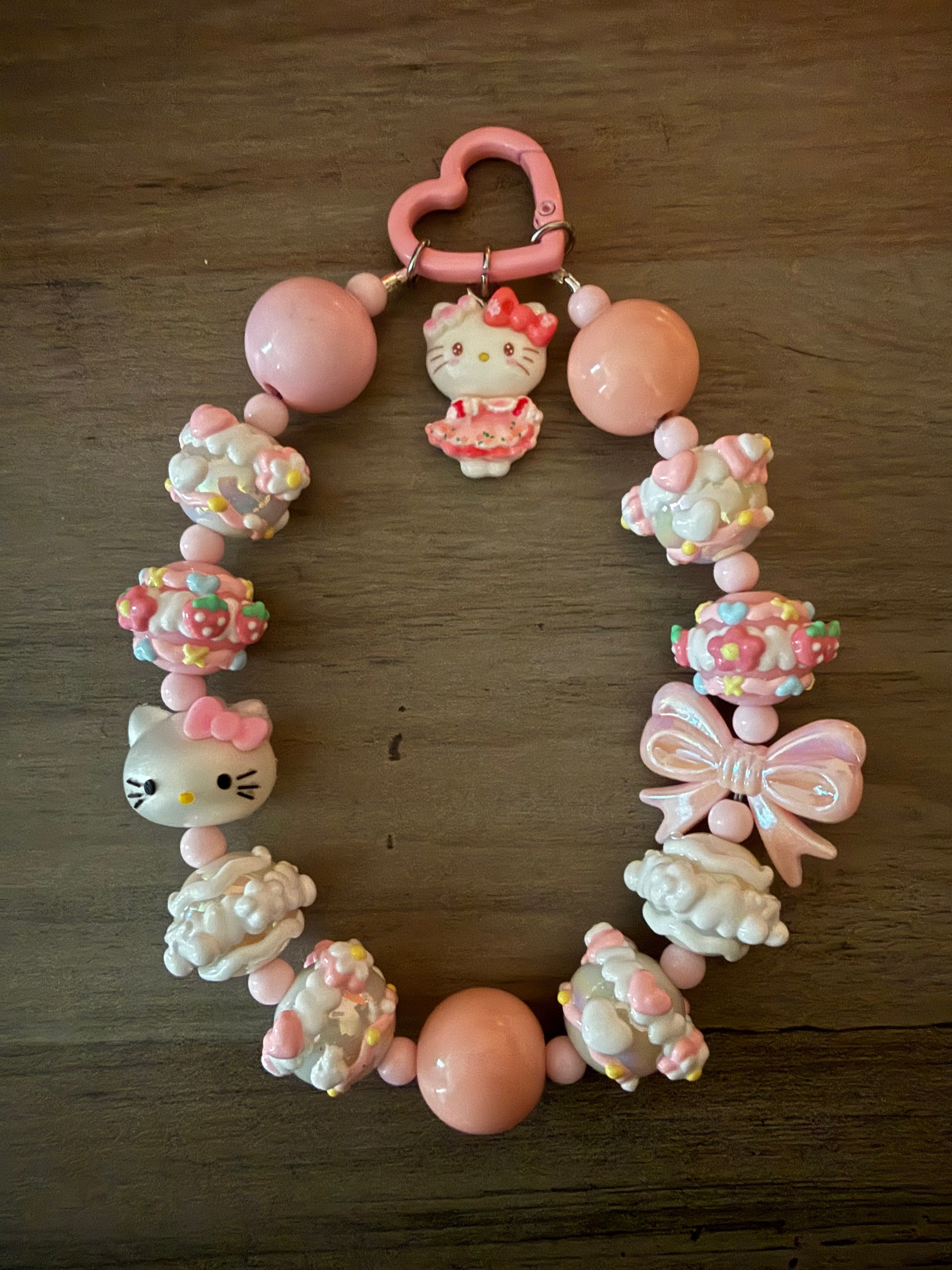 Colorful beaded keychain featuring a Hello Kitty inspired charm in a pink dress, decorative cupcake beads, a bow, and pastel-colored elements.