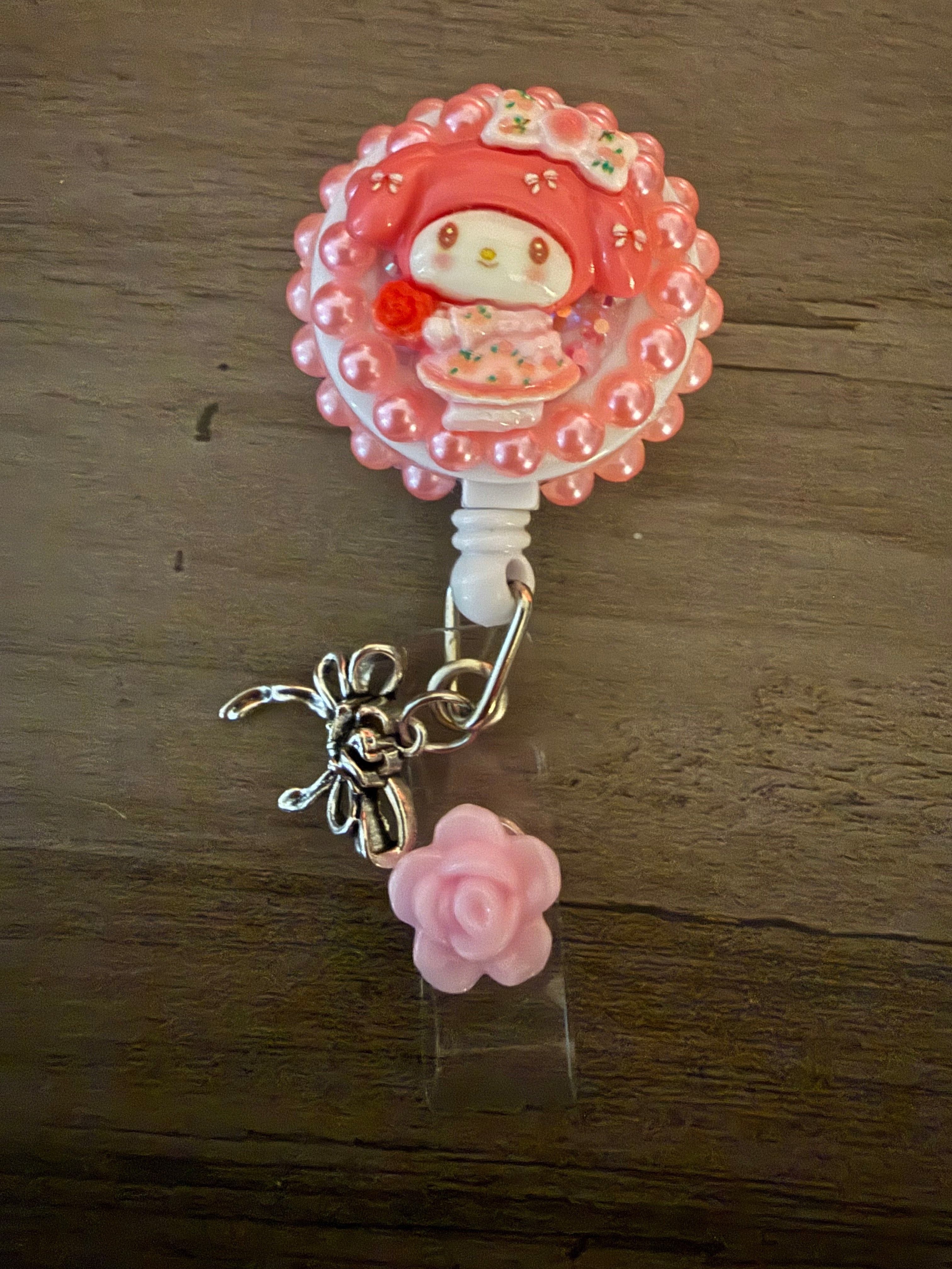 Colorful badge reel featuring a cute my melody inspired charm with a pink background, decorative beads, a silver butterfly charm, and a pink rose accent.