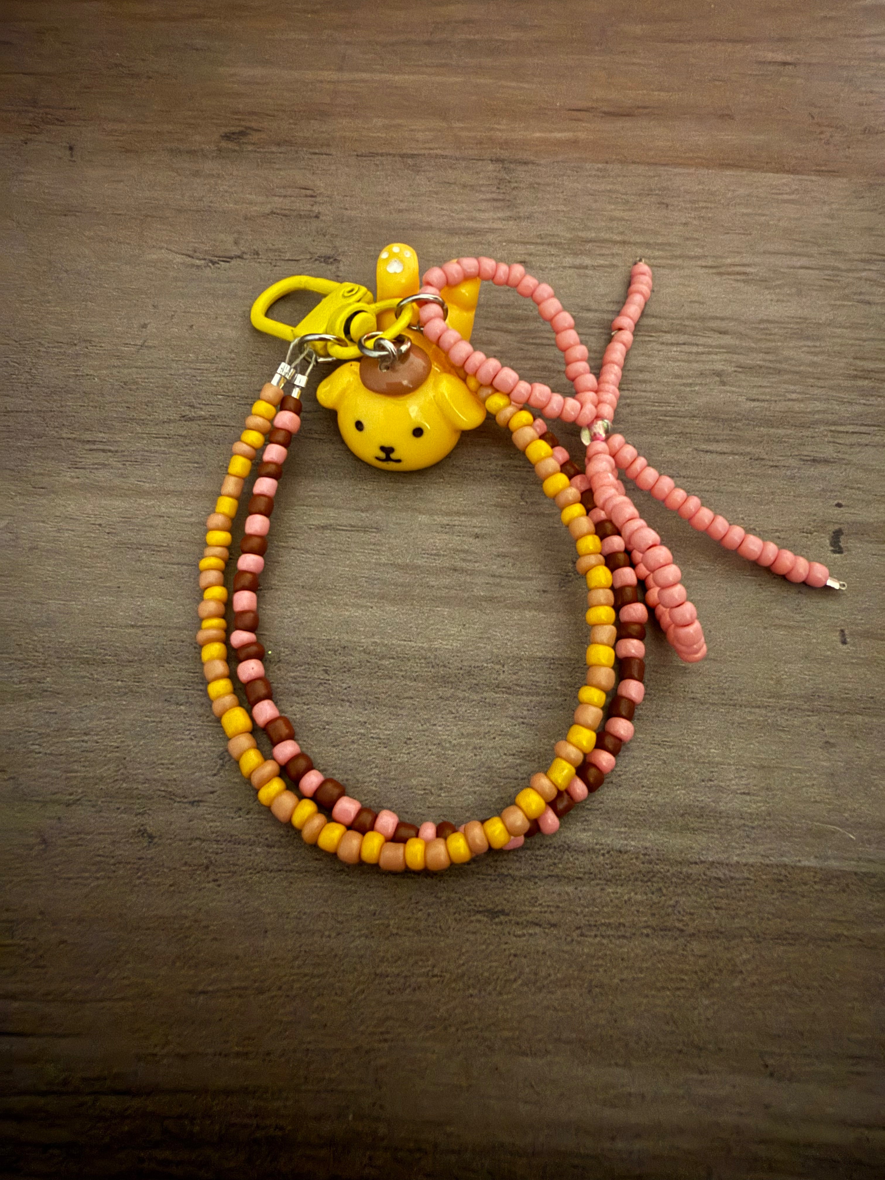 Handmade bag charm featuring a Pompompurin character charm on a beaded loop of yellow, brown, and tan seed beads.