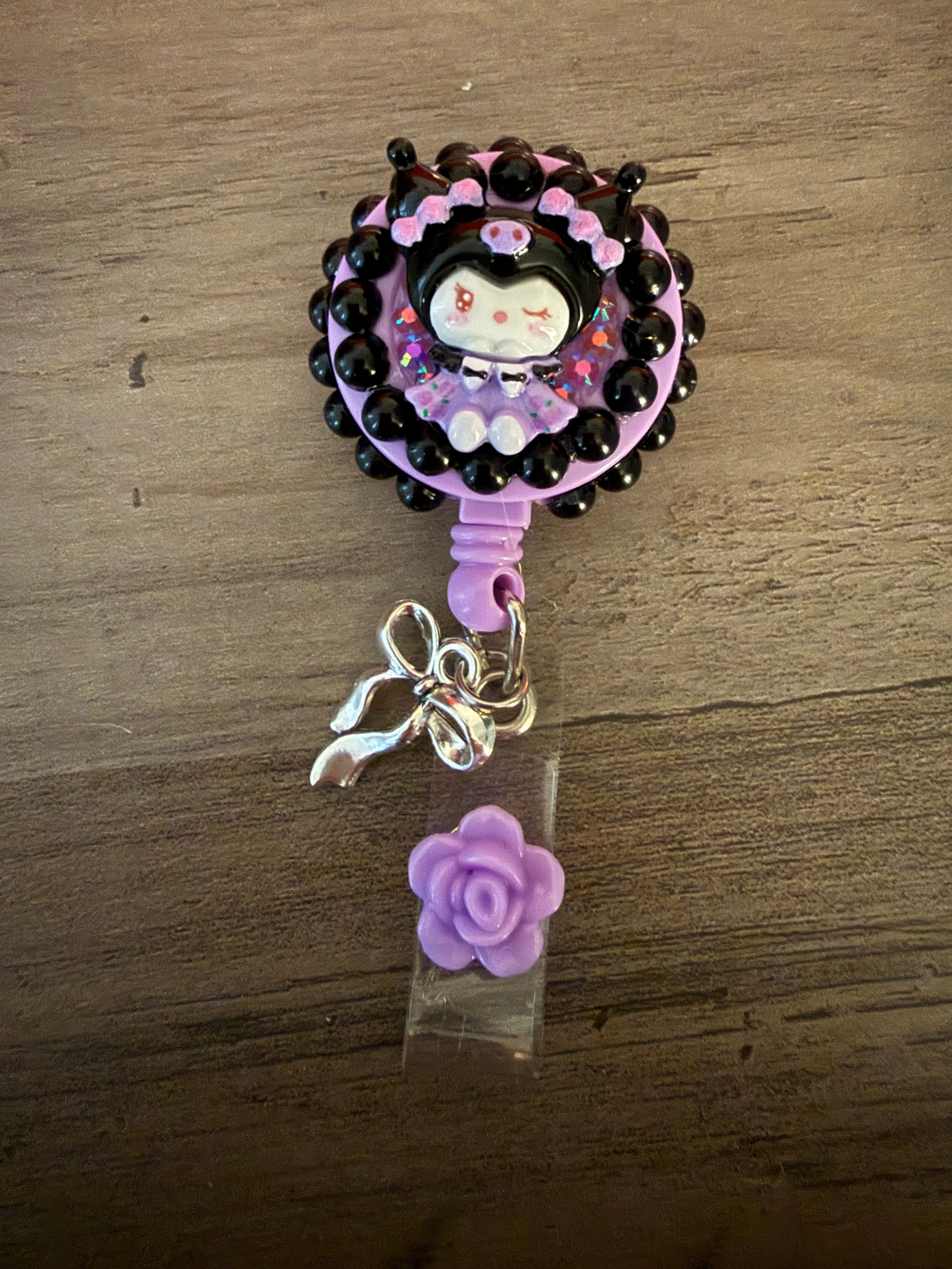 Colorful badge reel featuring a cute kuromi inspired charm with a black and purple design, surrounded by black beads, a silver bow charm, and a small purple rose accent.