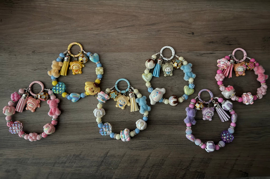 Six colorful beaded bag charms featuring Sanrio-themed charms, fuzzy bears, and decorative tassels.