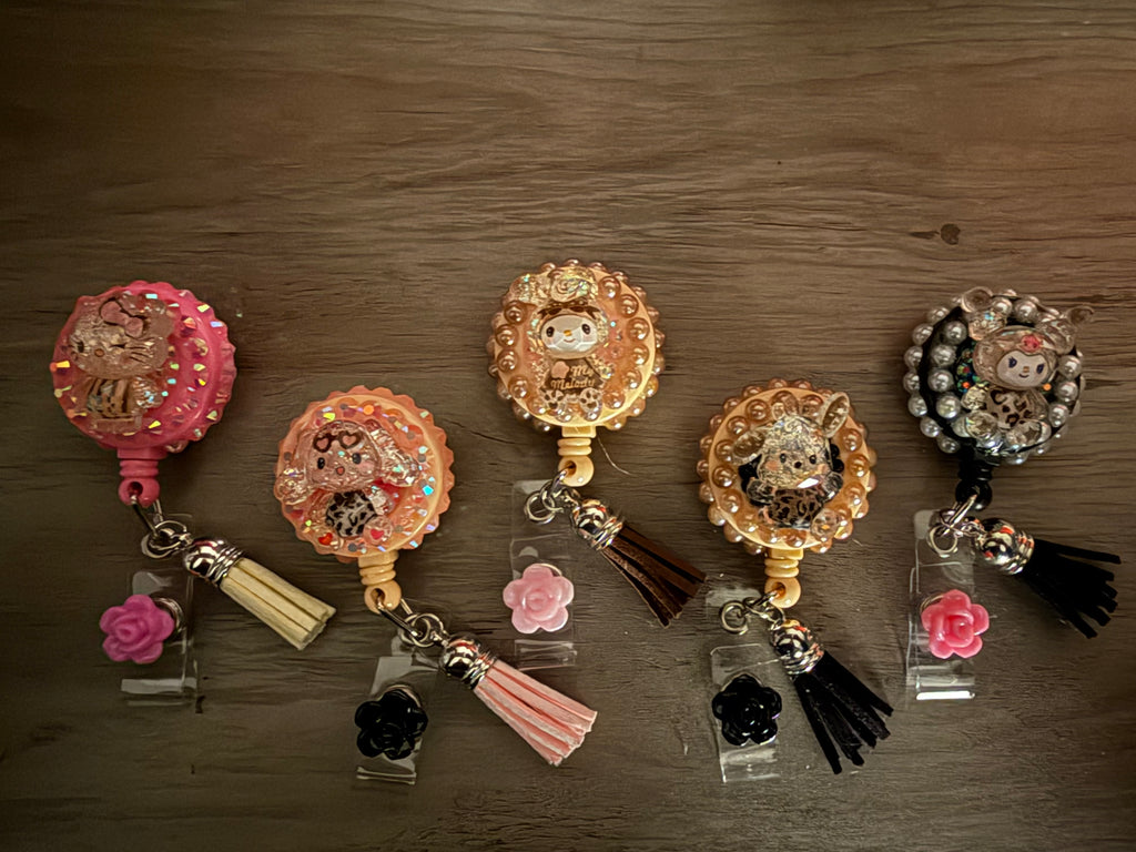 Five retractable badge reels decorated in a decoden style with Sanrio characters, featuring glitter, pearls, leopard and matching tassels.
