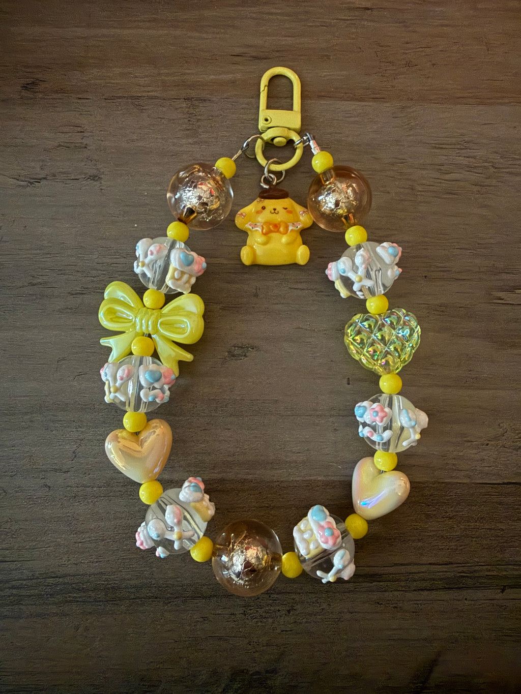 Colorful beaded keychain featuring a yellow pompompurin inspired charm, decorative bows, heart and round beads, and pastel accents.
