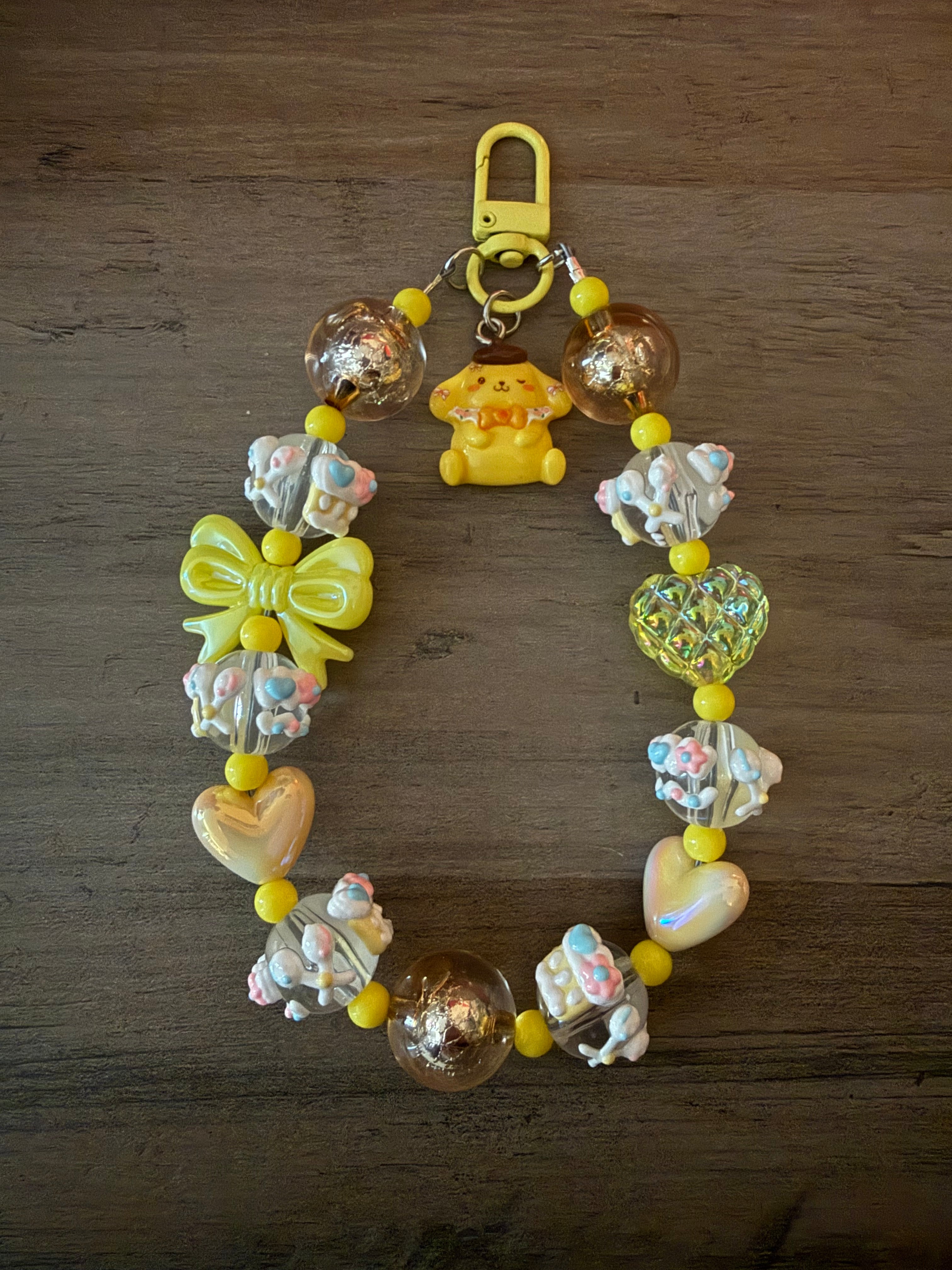 Colorful beaded keychain featuring a yellow pompompurin inspired charm, decorative bows, heart and round beads, and pastel accents.
