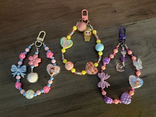 Three vibrant bag and phone charms, showcasing colorful beads, flowers, hearts, and playful characters in pastel shades.