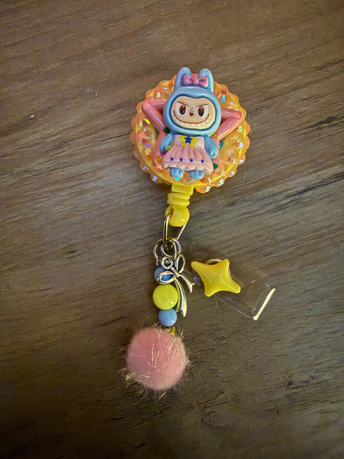 Colorful badge reel featuring a cute character, adorned with a pink pom-pom and playful charms.