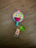 Colorful cupcake badge reel with a pink glitter base and a green heart charm.