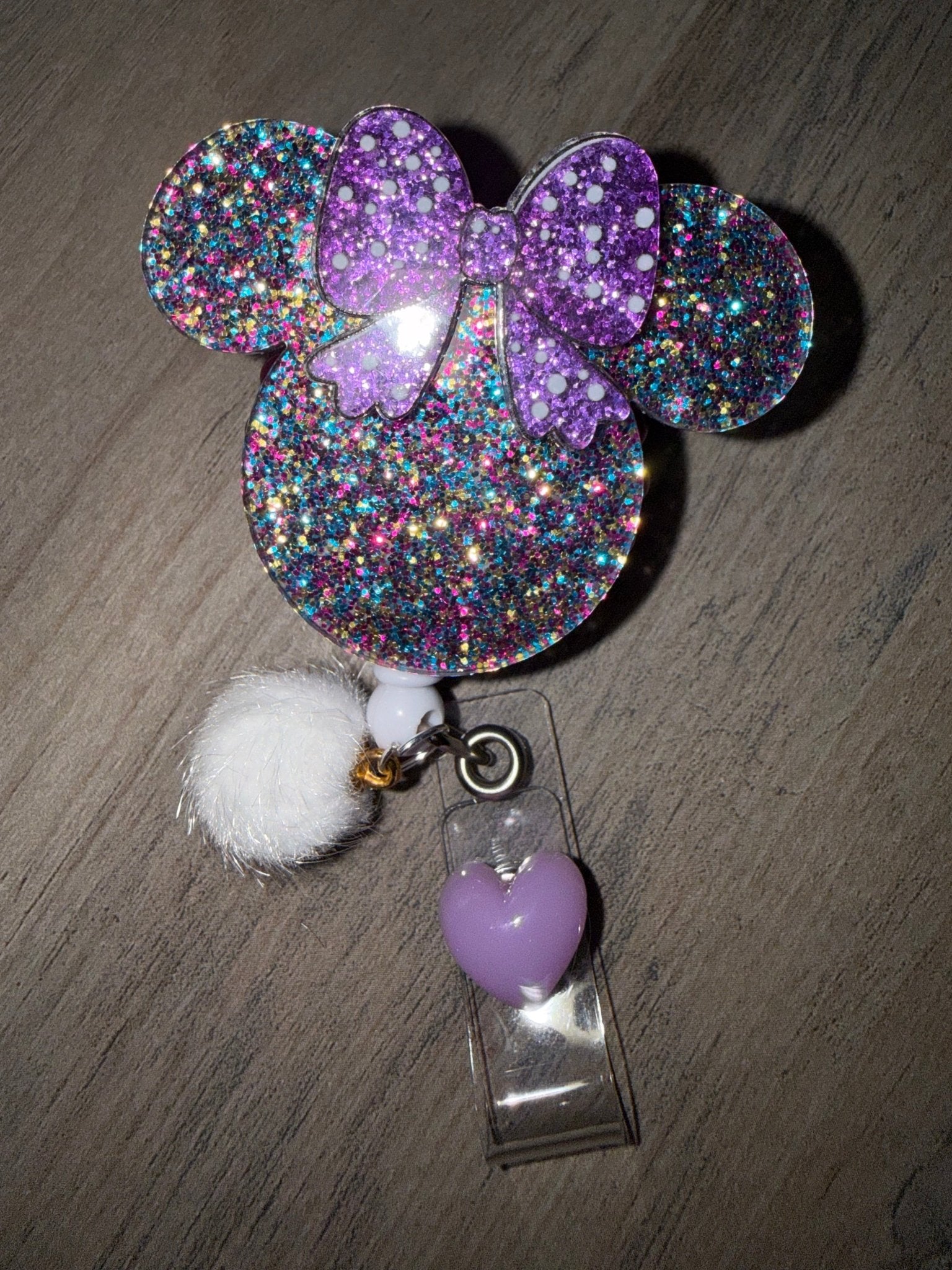 Handmade purple glitter Minnie Mouse badge reel with a white pom-pom and purple heart charm.