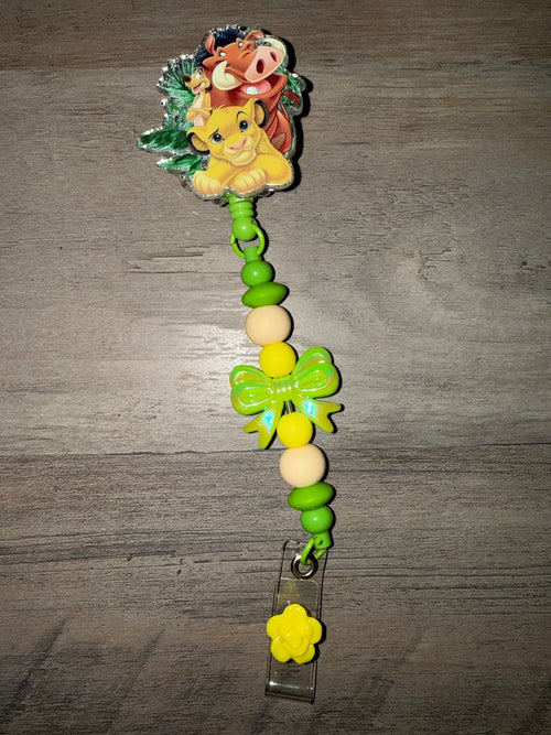 Handmade Lion King retractable badge reel with Simba, Timon, and Pumbaa, featuring green and yellow beads and a matching bow.