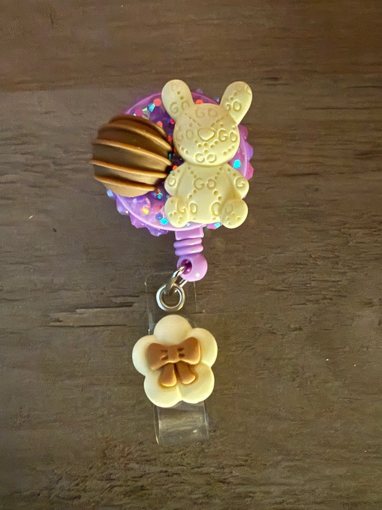 A purple badge reel featuring a cute bunny design with a chocolate treat and a small cream-colored flower charm with a bow.
