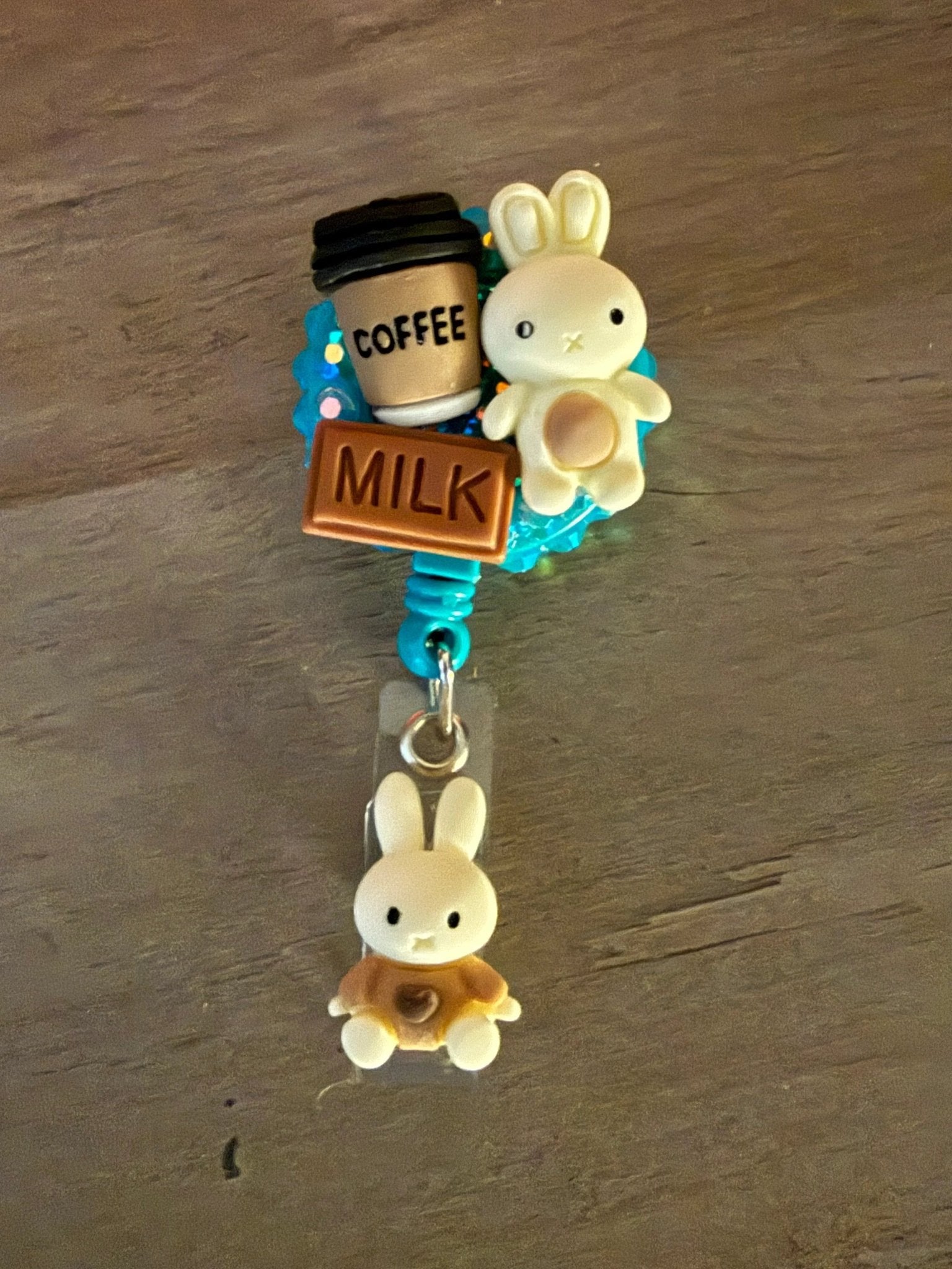 A colorful badge reel featuring a coffee cup, a "MILK" sign, and a cute bunny charm, with a smaller bunny charm below.