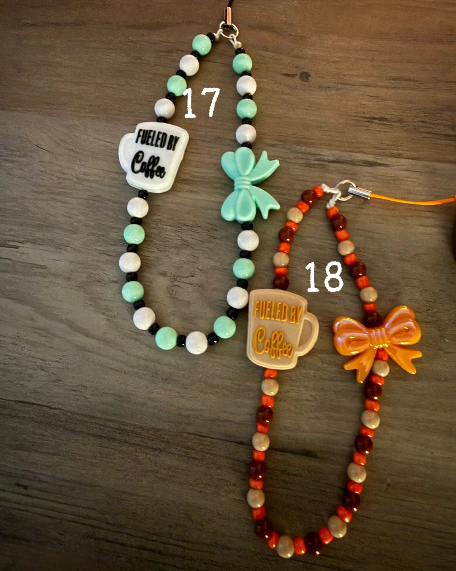 Two colorful coffee-themed phone charms with mug designs and bows, displayed on a wooden surface.
