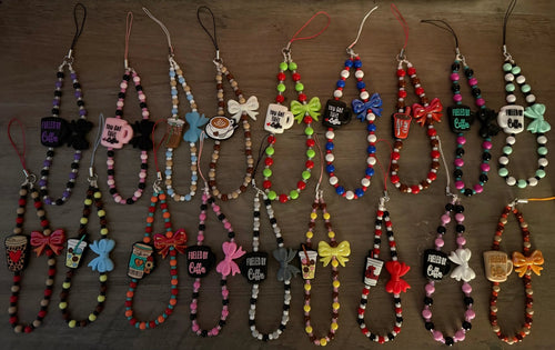 A colorful assortment of coffee-themed phone charms on a wooden surface, featuring various designs with beads, bows.