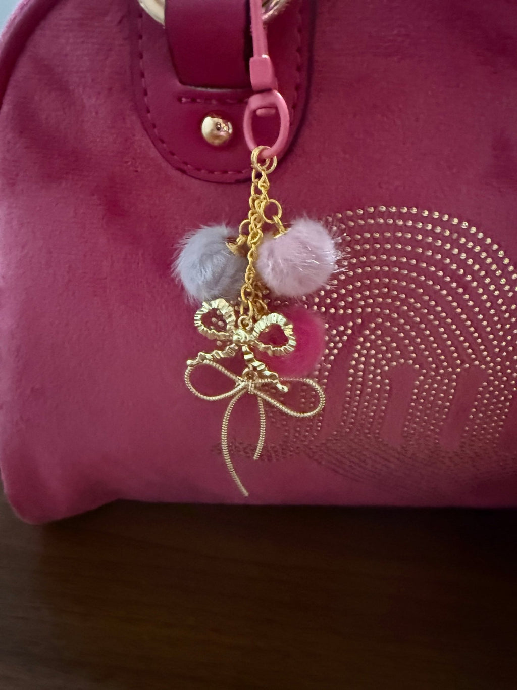 Handmade pink and grey fuzzy pom-pom bag charm with gold wire bows, shown attached to a pink velvet purse.