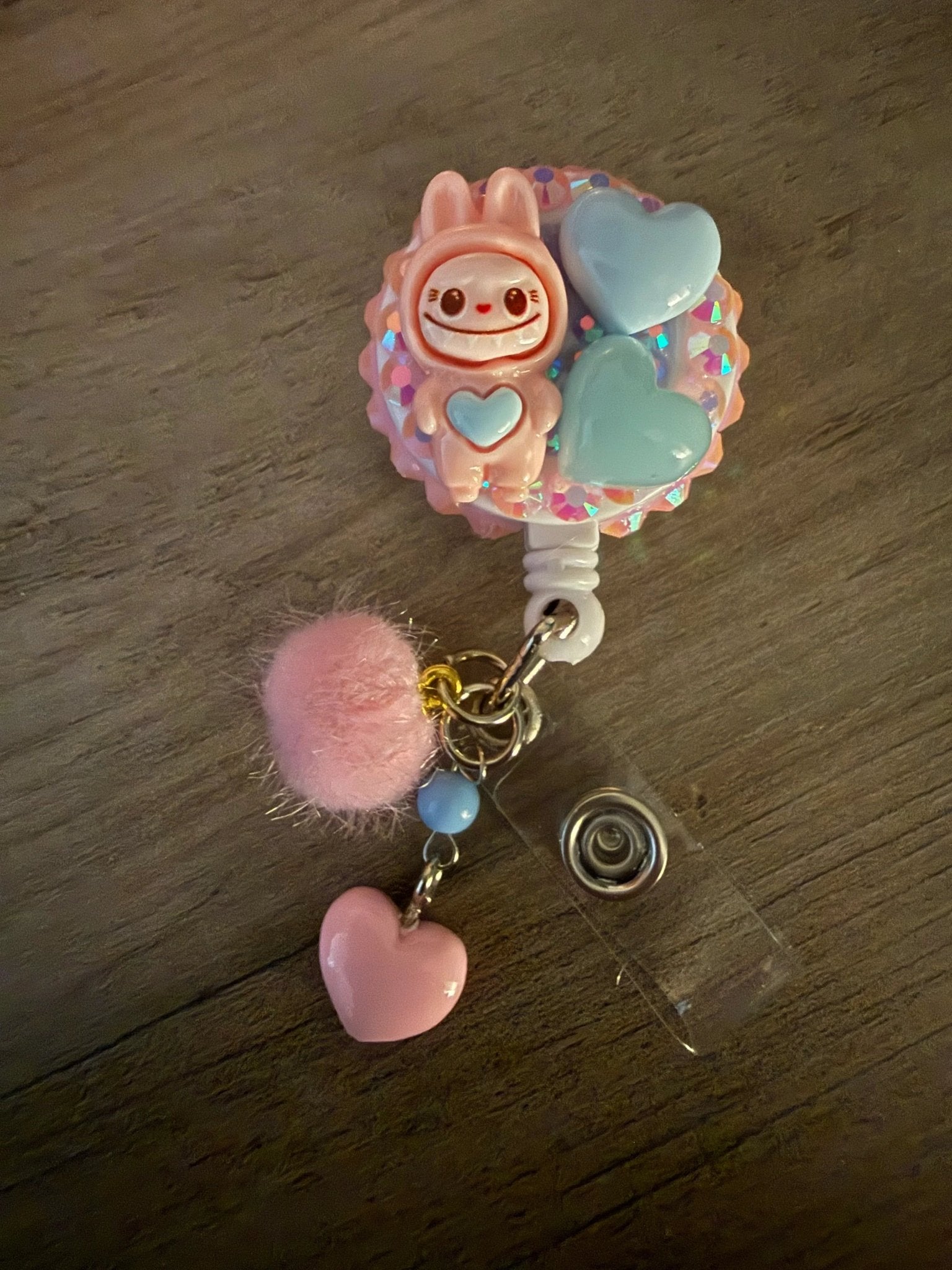 Cute badge reel featuring a pink monster character, two hearts, a pink pom-pom, and colorful charms.