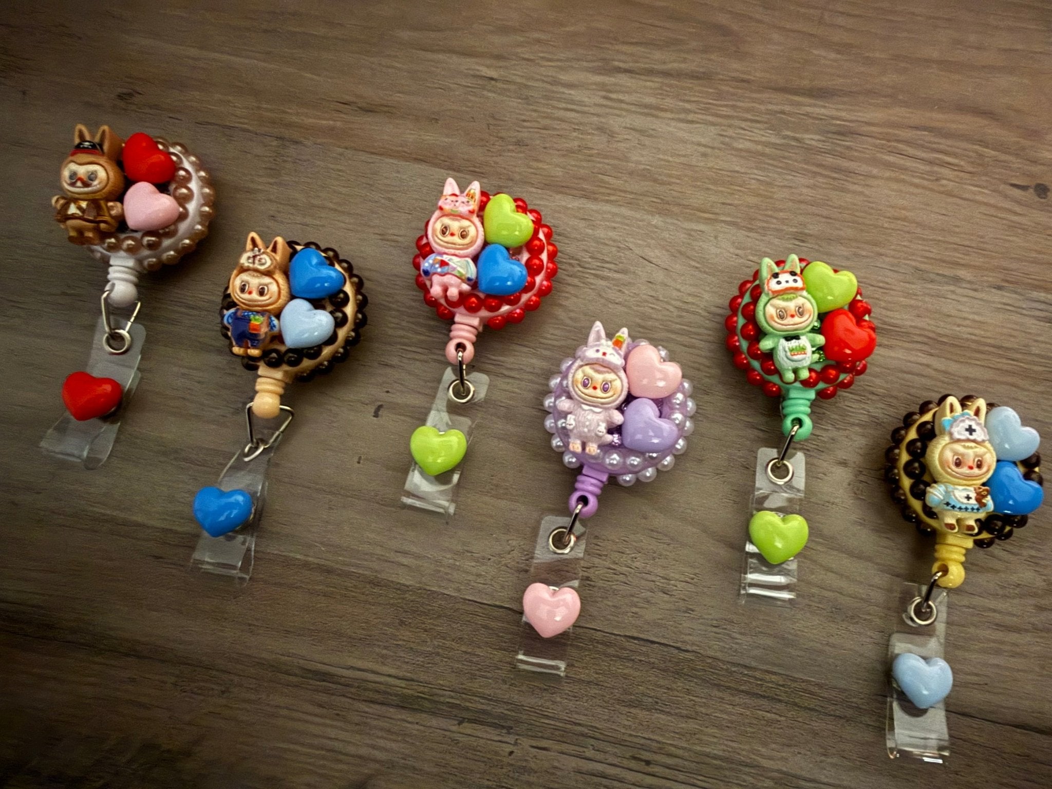 Six decorative retractable badge reels featuring various colorful character figures and heart charms.