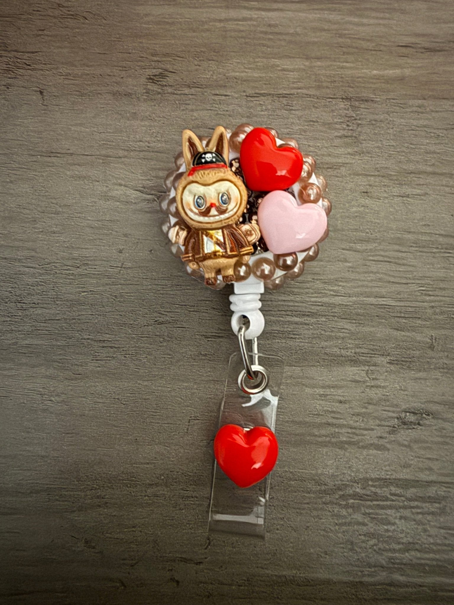 A decoden retractable badge reel featuring a pirate-themed character and red and pink heart charms.