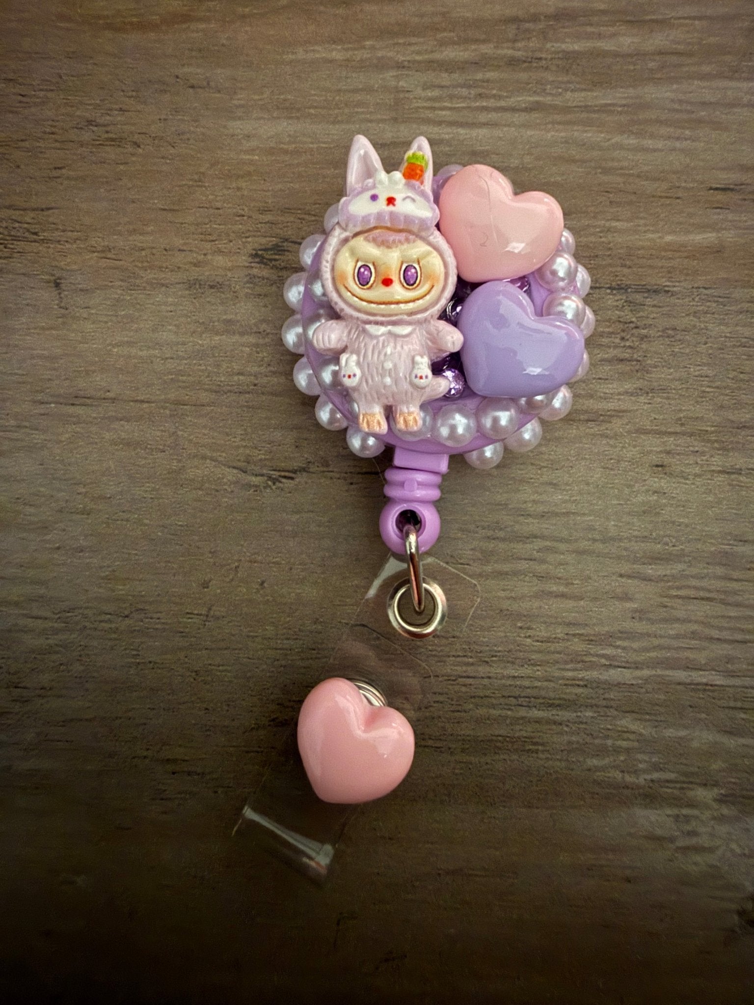 Decoden retractable badge reel featuring a purple bunny character with pink and purple heart charms on a white pearl base.