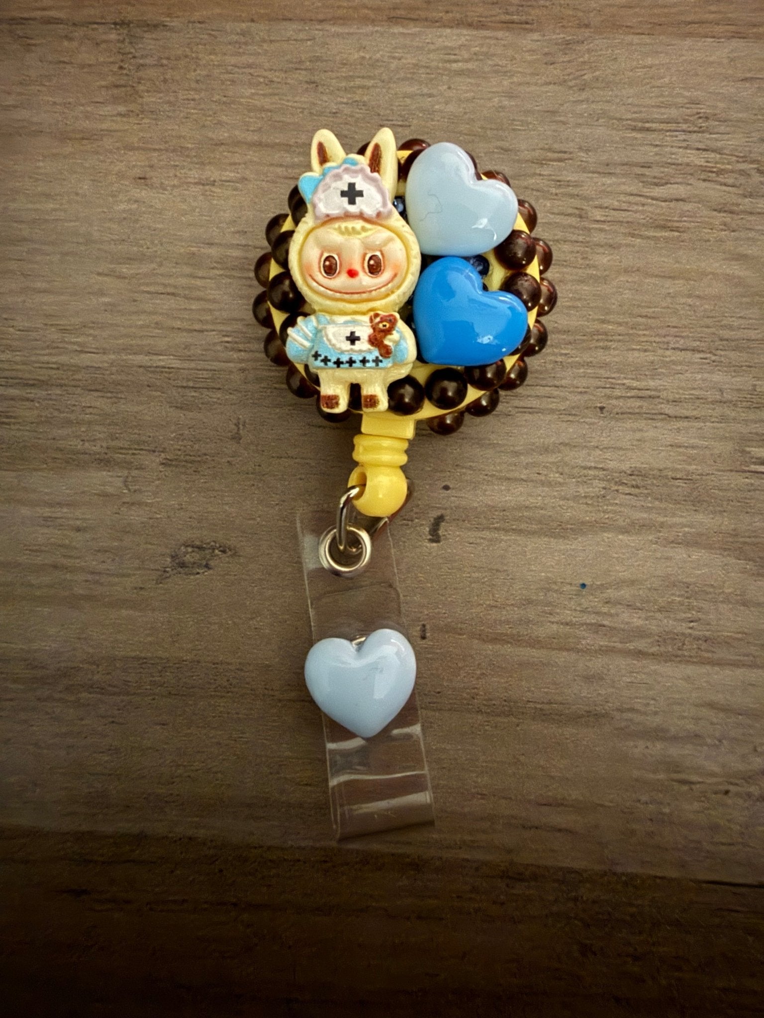 Decoden retractable badge reel featuring a nurse-themed character with blue heart charms on a dark beaded base.