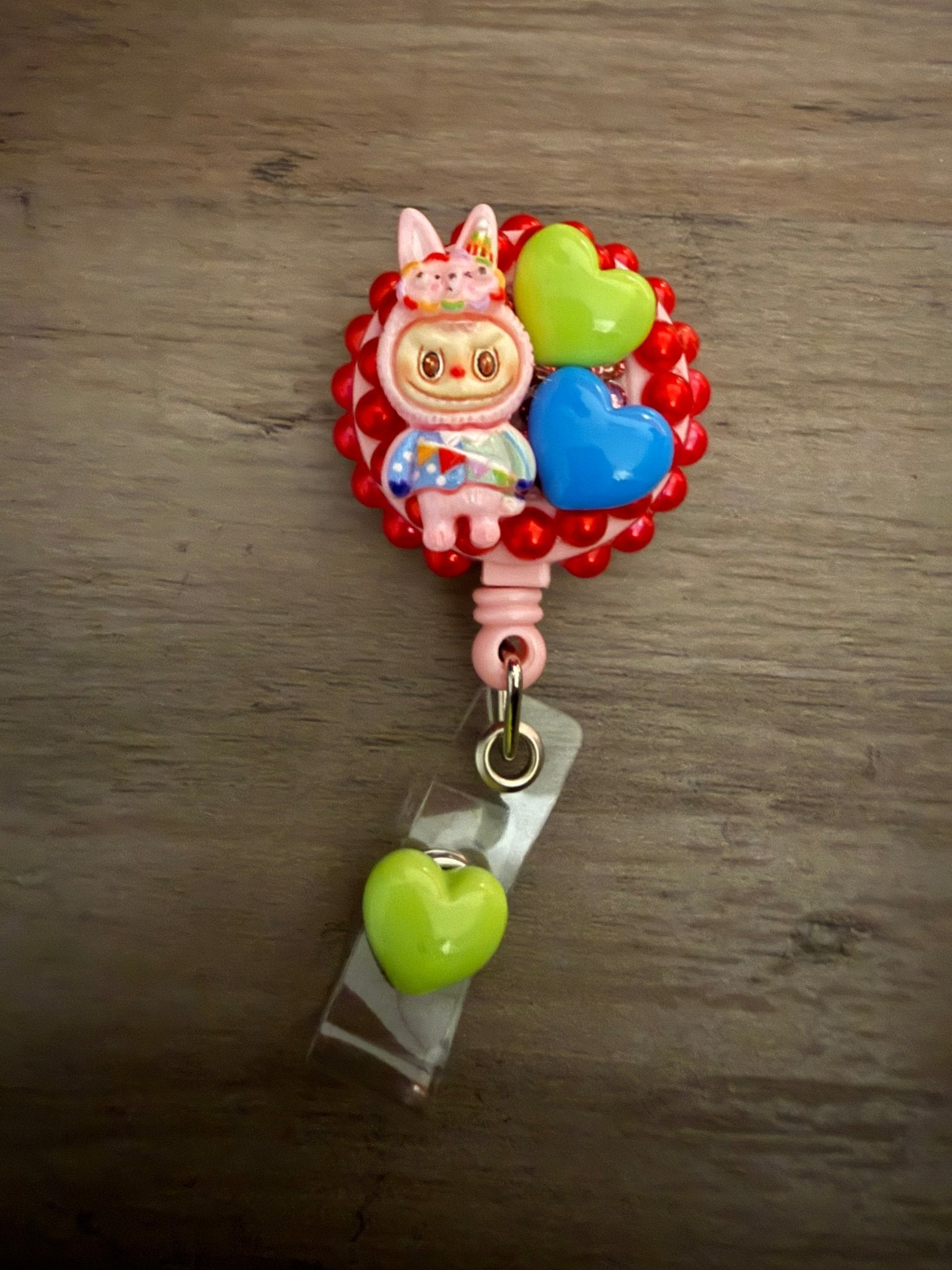 Decoden retractable badge reel featuring a pink bunny character with green and blue heart charms on a red beaded base.