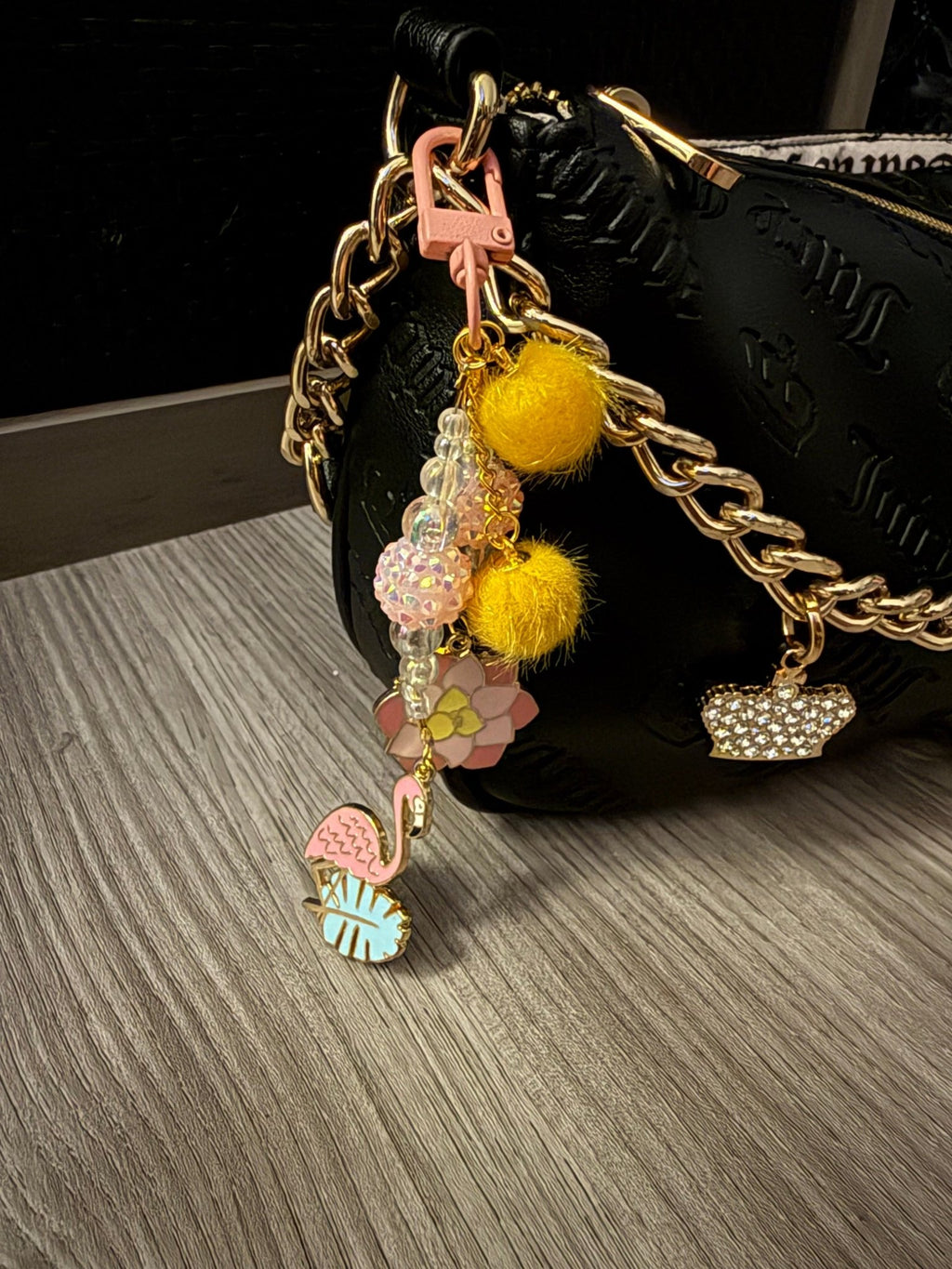Tropical bag charm attached to a black purse, featuring a pink flamingo, lotus flower, yellow pom-poms, and iridescent beads.