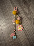 Handmade tropical beaded keychain with a pink flamingo charm, a lotus flower charm, yellow pom-poms, and pink glitter beads.