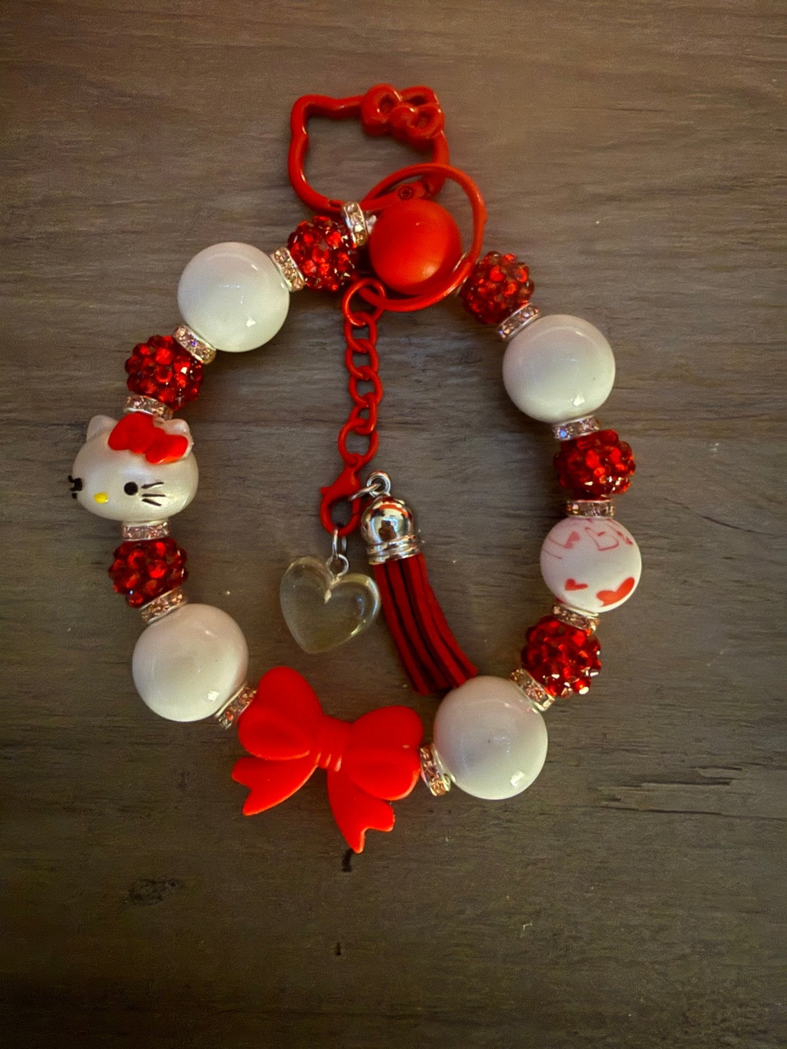 Handmade red and white Hello Kitty beaded wristlet with rhinestone accents, a tassel, heart charm, and a red character clasp.
