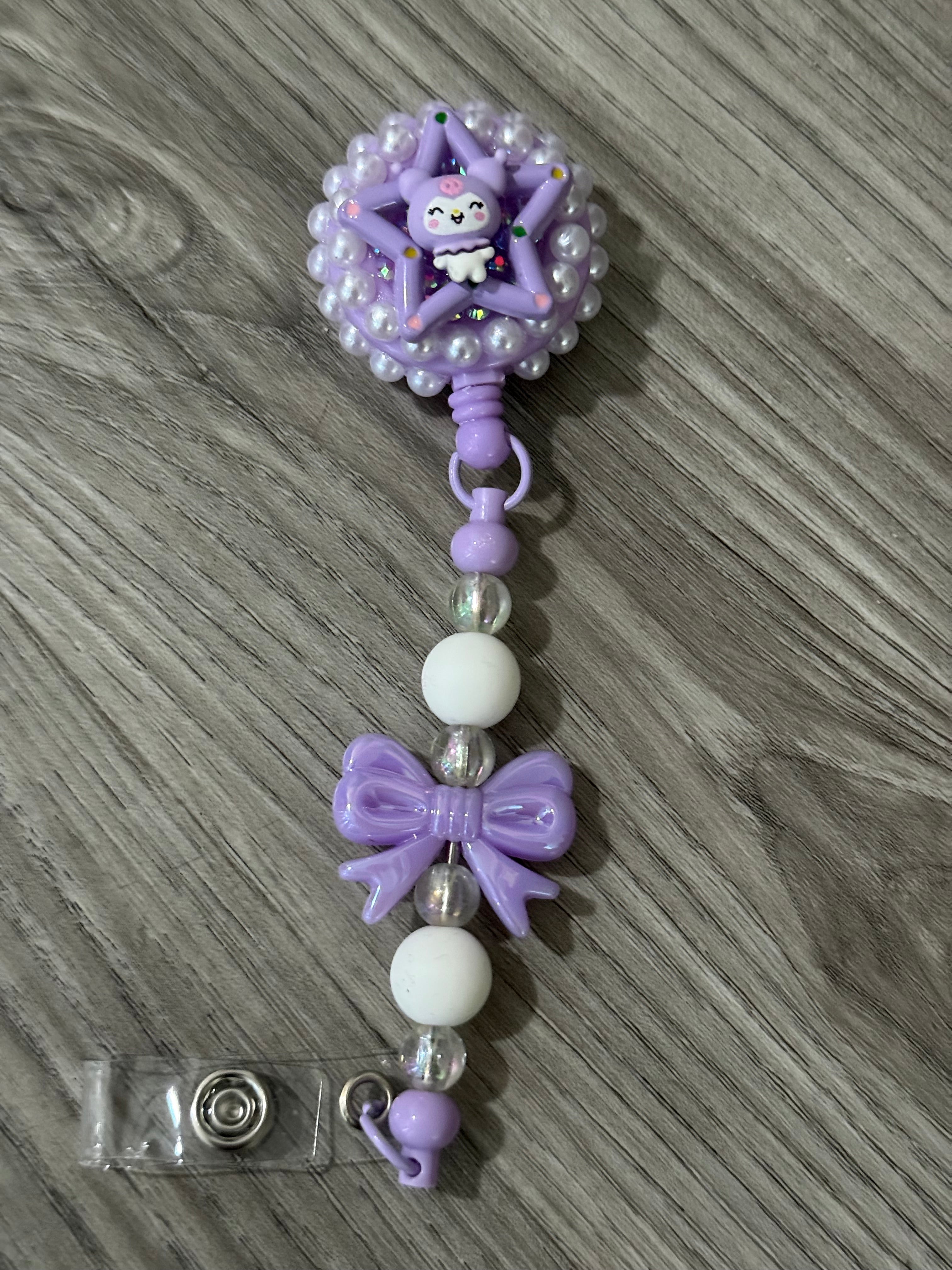 Cute badge reel featuring a whimsical design with a purple star-shaped top, adorned with a cheerful kuromi inspired character and surrounded by pearl-like beads, complemented by a decorative purple bow and colorful beads on the strap.