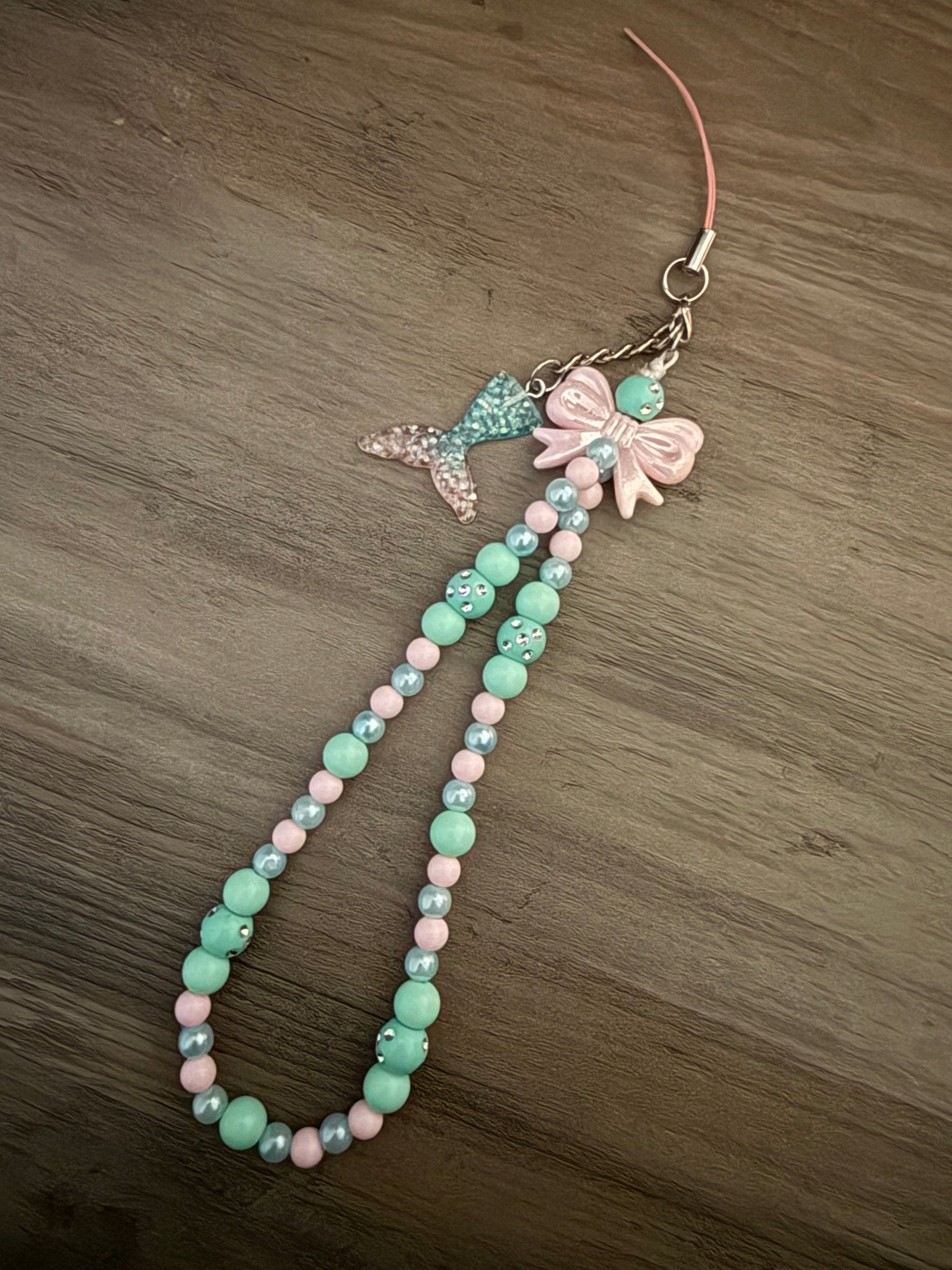 Handmade mint and pale pink beaded phone wristlet with a mermaid tail charm and a pink bow.