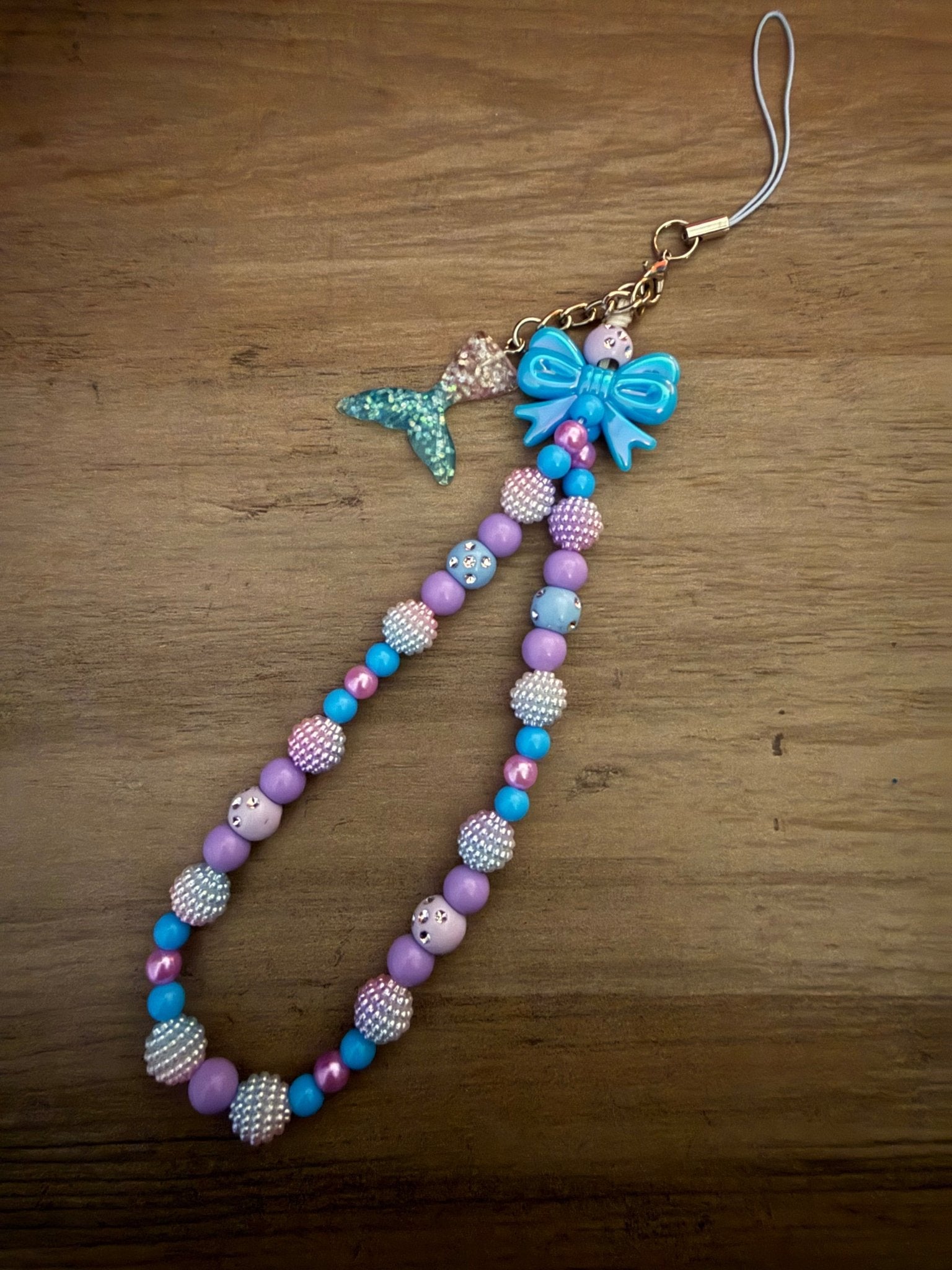 Handmade purple and blue beaded phone wristlet with a mermaid tail charm and a blue bow.