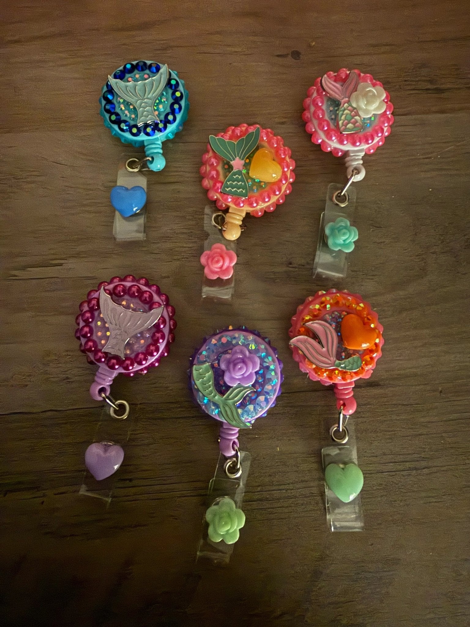 A collection of six colorful badge reels with mermaid and flower designs, with beads and small charms in various colors.
