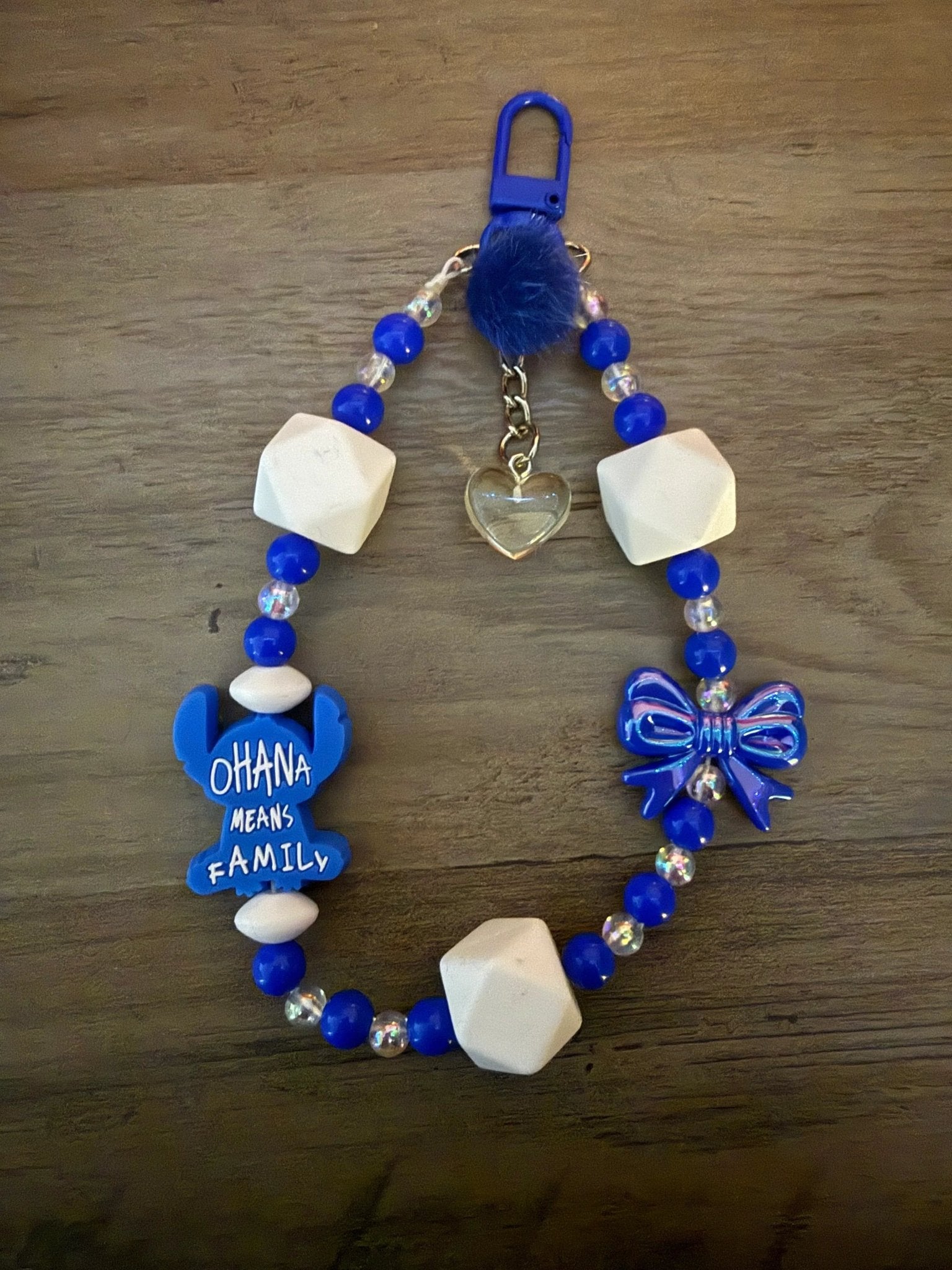 Blue "Ohana means family" bag charm/phone charm with character charm, heart charm, white beads, and a fluffy pom-pom.
