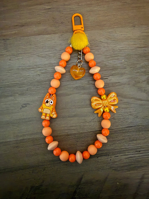 Orange bag charm/phone charm with character charm, yellow pom-pom, heart charm, and decorative beads.