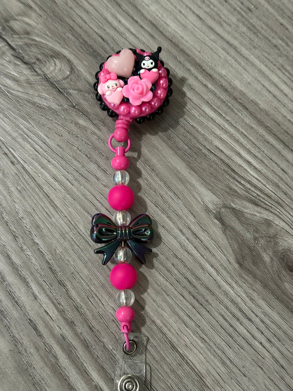 Cute badge reel featuring a playful design with pink and black accents, adorned with charming kuromi and my melody inspired characters, roses, and a decorative bow.
