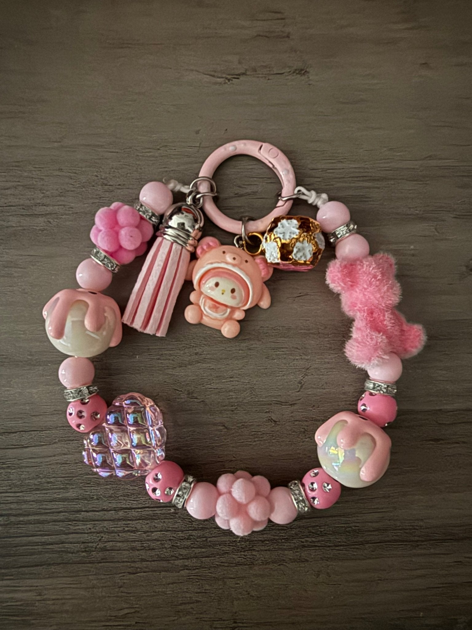 A pink beaded bag charm/phone charm featuring a My Melody charm, a fuzzy bear, a tassel, and various textured beads.
