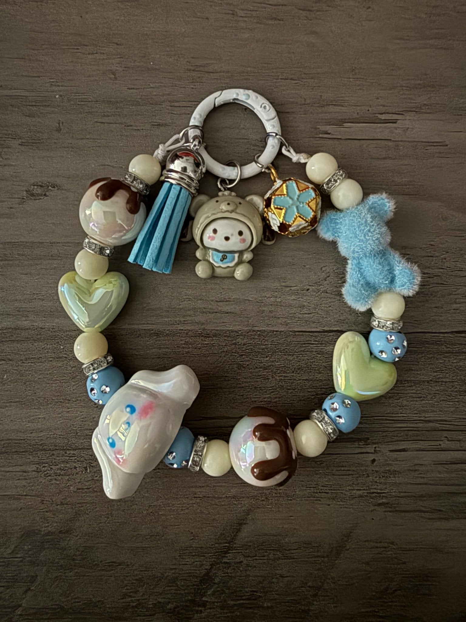 A pastel blue and green beaded bag charm/phone featuring Pochacco and Cinnamoroll, a fuzzy blue bear, and a blue tassel.