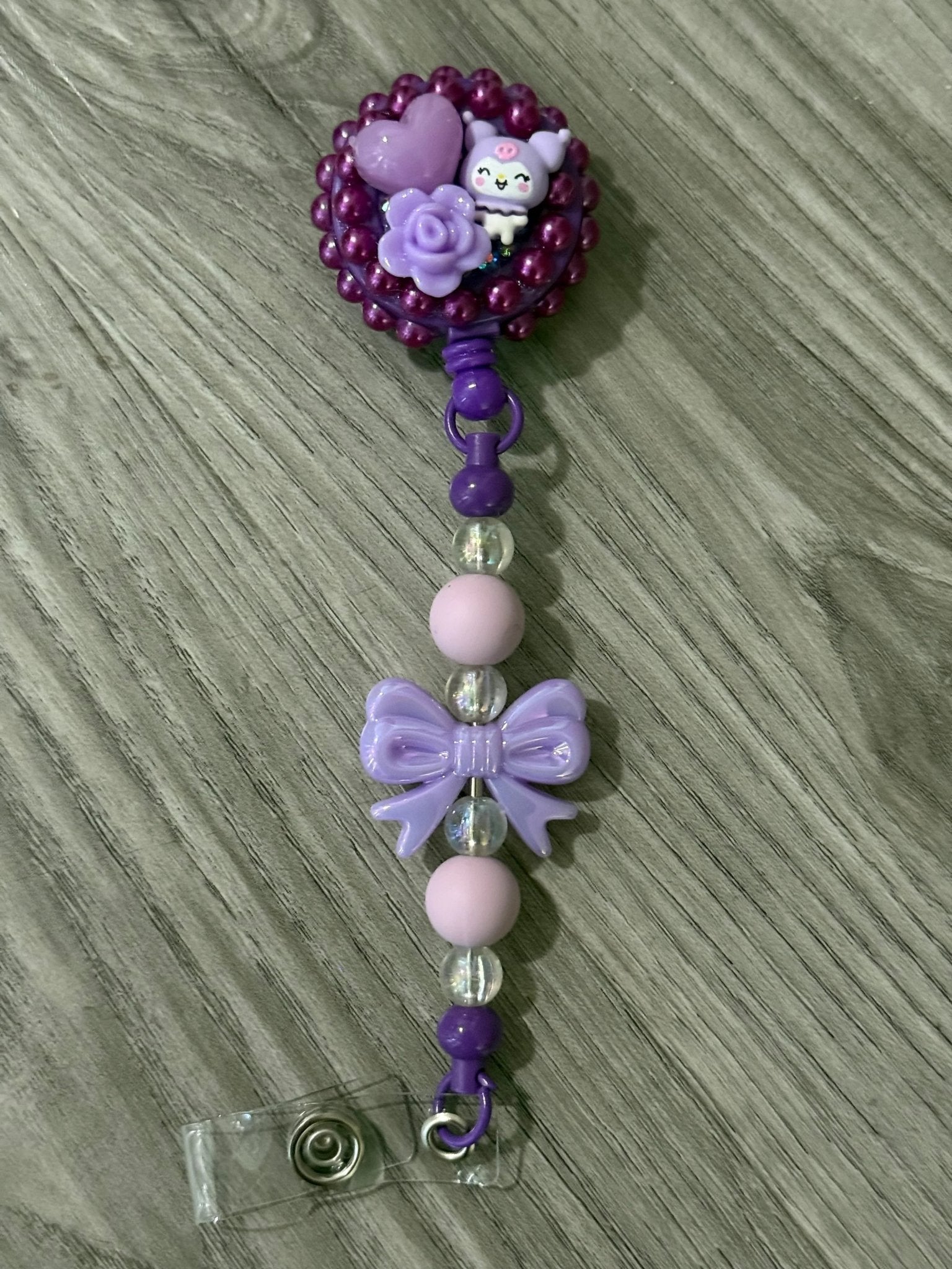 A purple badge reel with a cute character, a heart, and a rose, beaded strap with a purple bow and pink beads.