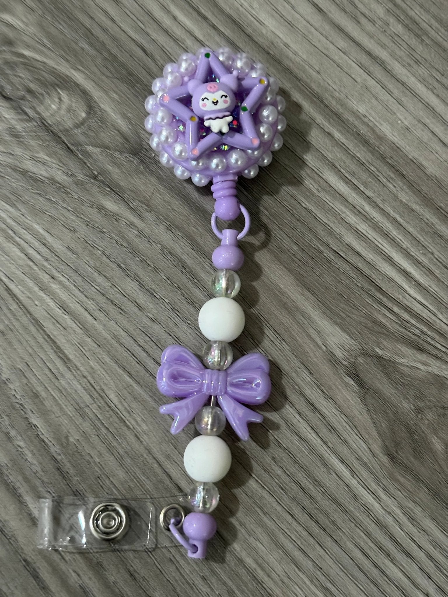 A whimsical purple badge reel with a cute design, pearl-like beads, and a beaded strap with purple bow and white beads.